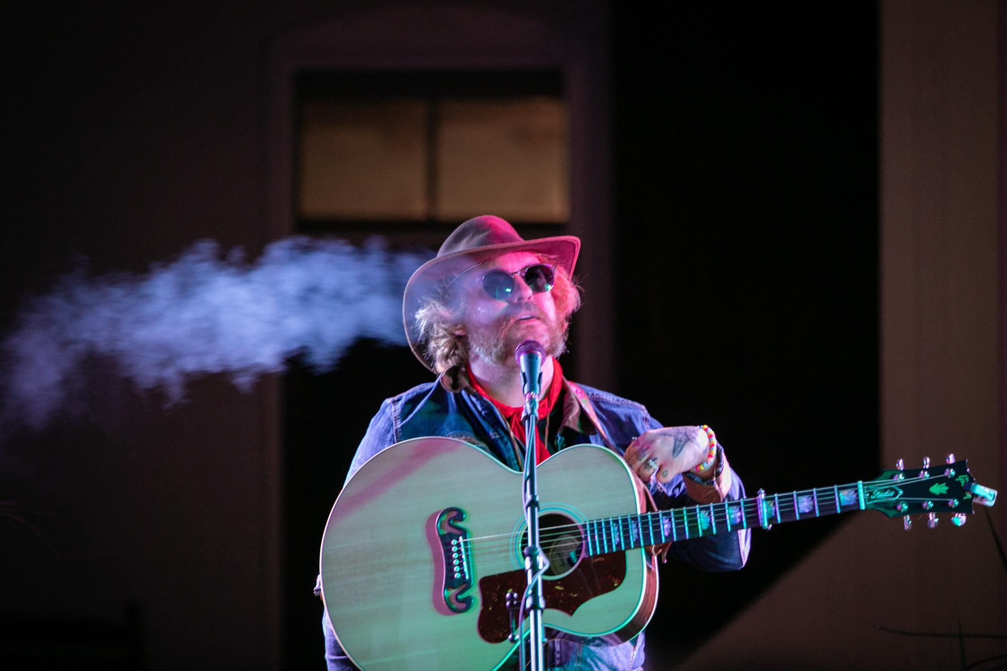 Photograph of Adeem the Artist at night, smoking and standing in front of a microphone.