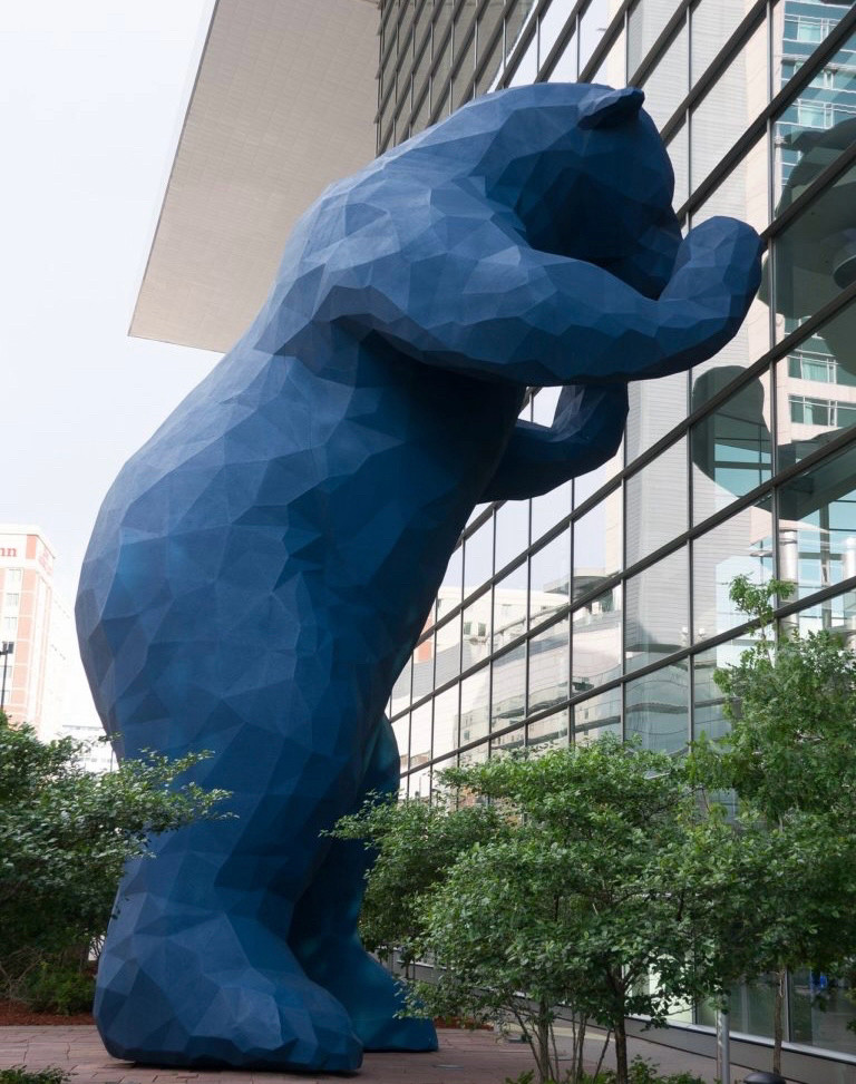 A giant blue 40 ft sculpture of a bear peering into a building