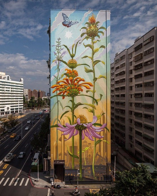Photo of the side of a multistorey building which features a large-scale mural of pink and orange flowering wild plants