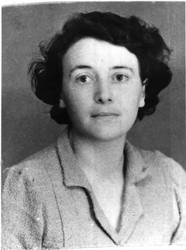 Monochrome photograph featuring the head and shoulders of a white woman facing forwards with dark wavey hair wearing a blouse