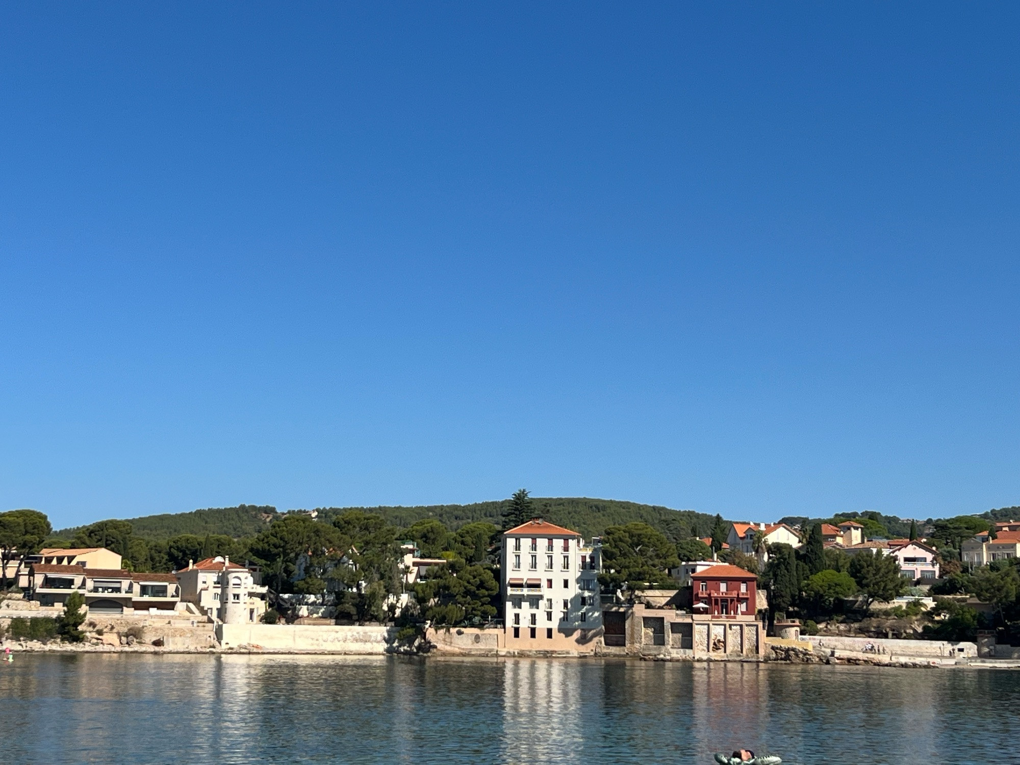 La plage de Rènecros à Bandol.
Ciel très bleu, des maisons de bord de mer et une mer transparente.