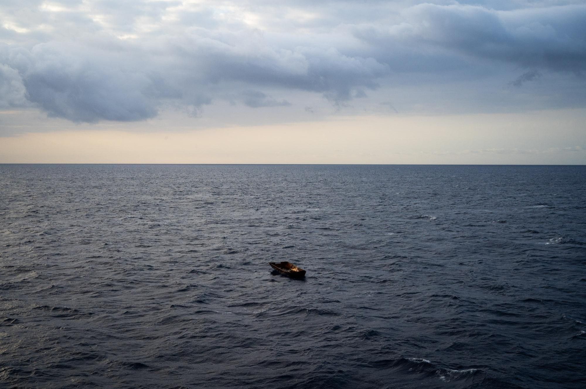 Ein kleines, leeres Eisenboot treibt auf weiter, leicht gekräuselter See unter Wolken.