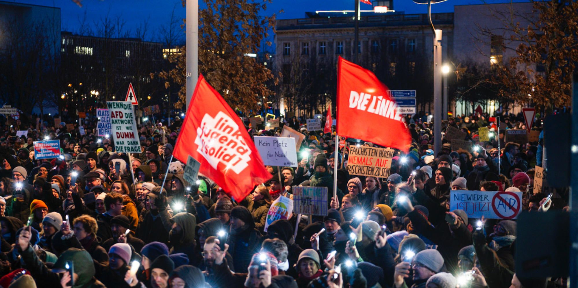 Eine Linkspartei- und eine Linksjugend-Solid-Fahne auf einer abendlichen Großdemonstration.