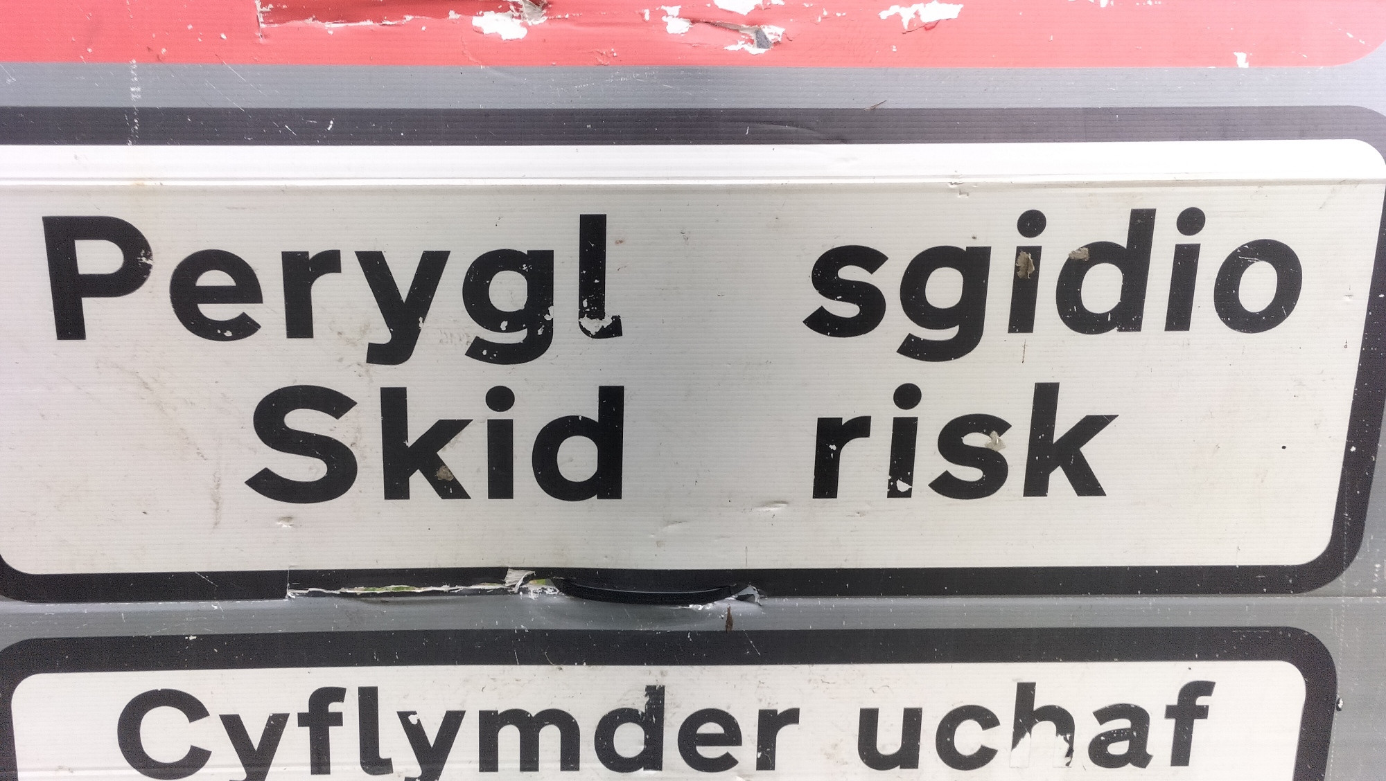A bilingual road sign that says:
Perygl sgidio 
Skid risk

Cuflymder uchaf. 