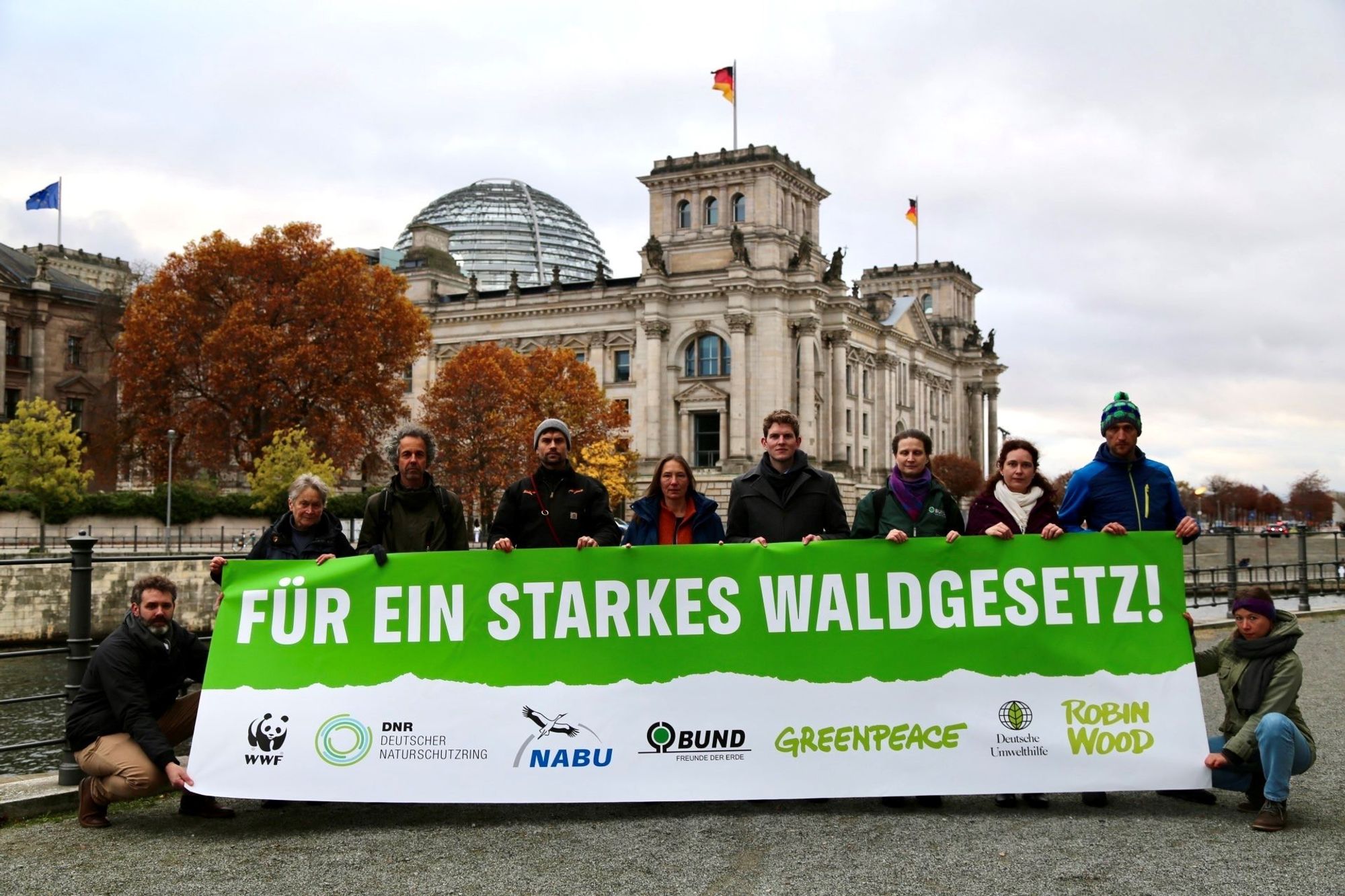 Vor dem Reichstagsgebäude steht eine Gruppe mit Vertreter*innen von Umweltschutzorganisationen. Sie halten ein Banner auf dem steht: Für ein starkes Waldgesetz!