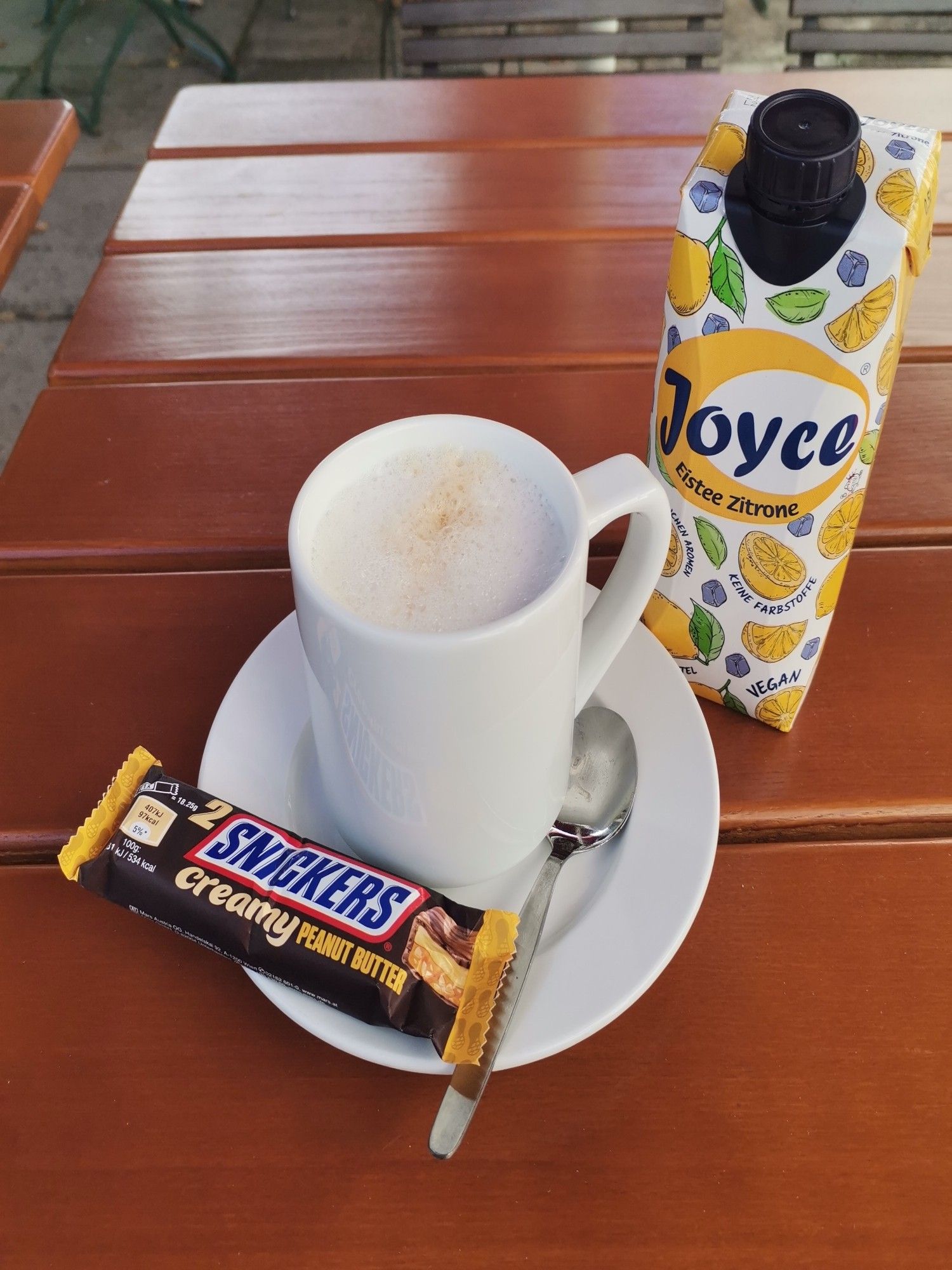 A cup of coffee on a brown table. Snickers and ice tea.