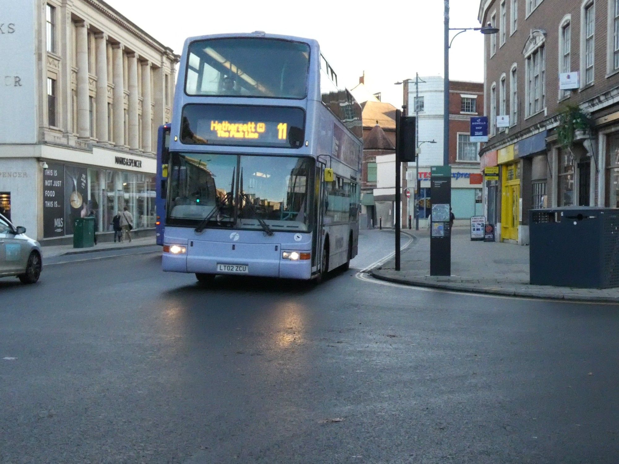 Lilac and white double deck bus on city street. Destination screen reads "11 Hethersett - The Pink Line"