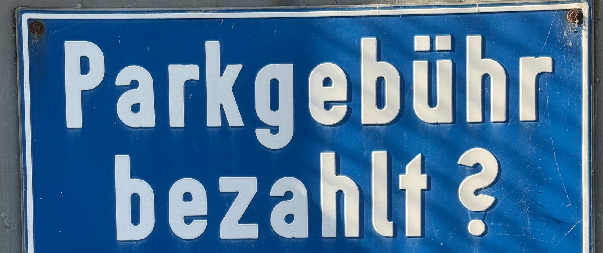 Ein blaues Schild mit weißem Text mit der Frage: "Parkgebühr bezahlt?"