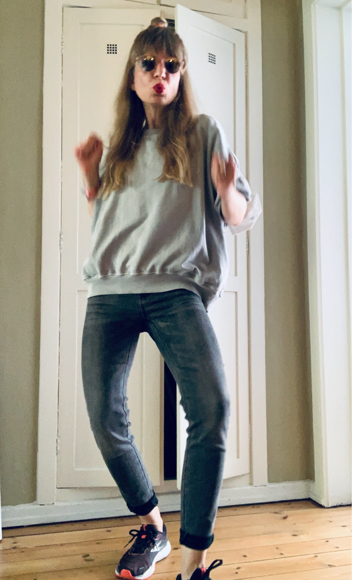 Ich vor den HarryPotter-Zimmer in dunkelgrauer Jeans und Oversize-T-Shirt in hellgrau mit kleinem Antennenteildutt und Sonnenbrille. Lippenstiftfarbe: Ruby Woo. Laufschuhe in Schwarzweiß und Neonorange