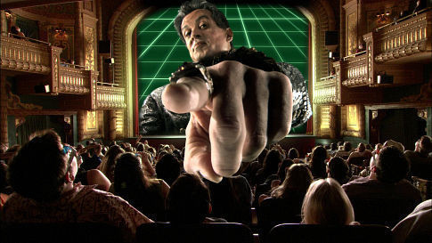 Sylvester Stallone pointing his finger out of a movie screen in 3d at some hapless people in a movie theater 