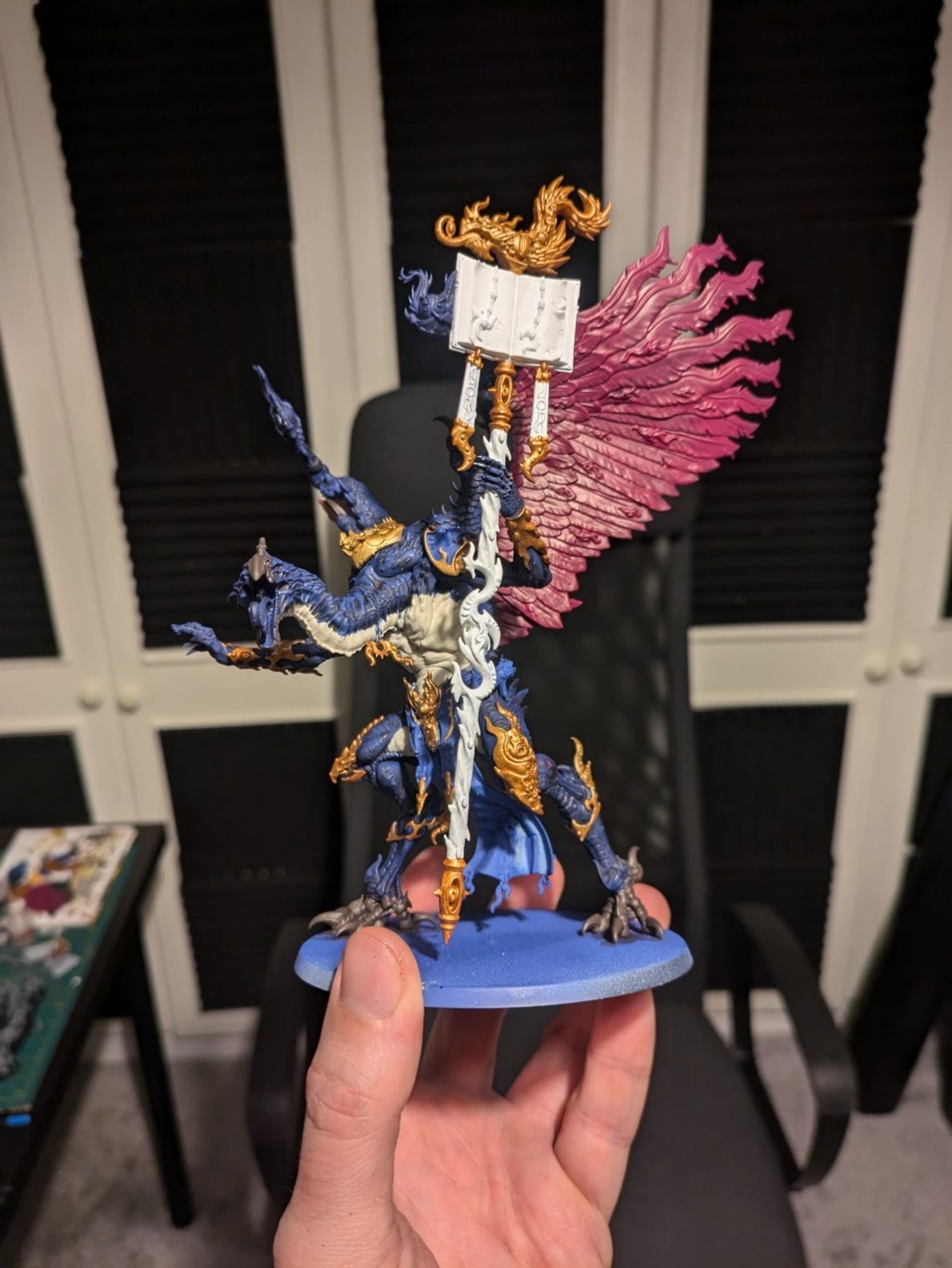 A photo of the Lord of Change Warhammer model I'm working on (big feathery winged bird demon holding a mystical staff) showing the blue, gold, pinky-purple, wraith one and dryaf bark base coats