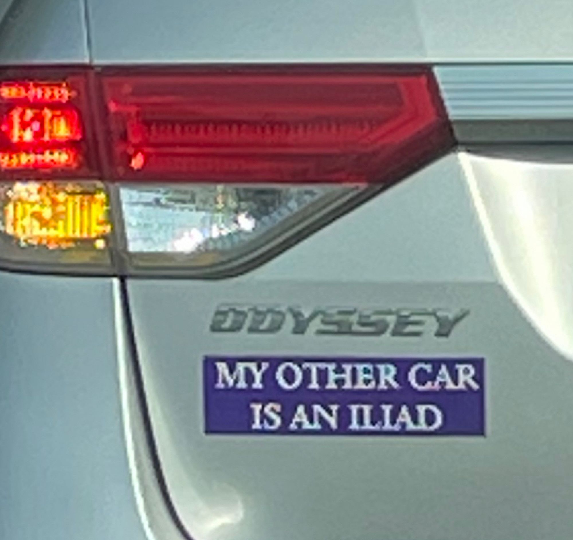 A bumper sticker just below where the car says Odyssey reading “my other car is an Iliad”