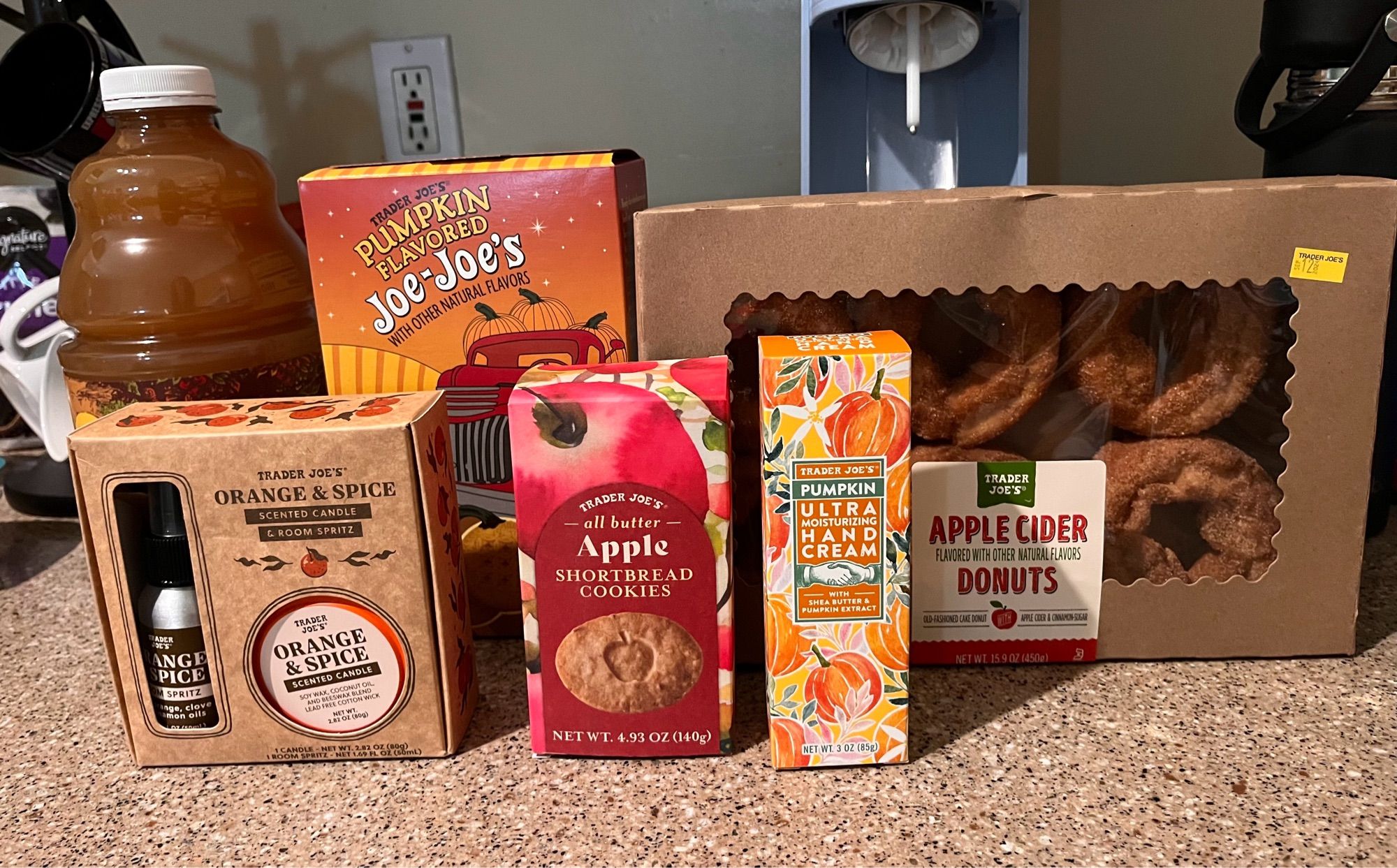 Selected fall themed Trader Joe’s products: orange spice room spray and candle, apple shortbread cookies, pumpkin handcream, spiced apple cider, pumpkin Joe-Joe’s sandwich cookies, apple cider donuts