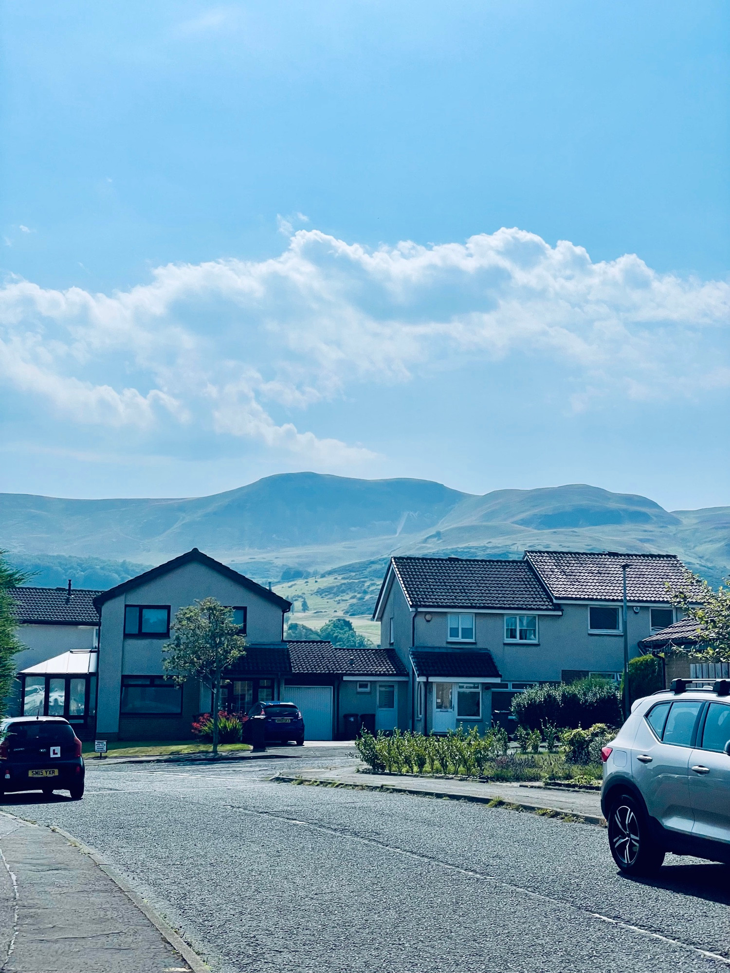 A view of the Pentlands hills behind some houses and cars.