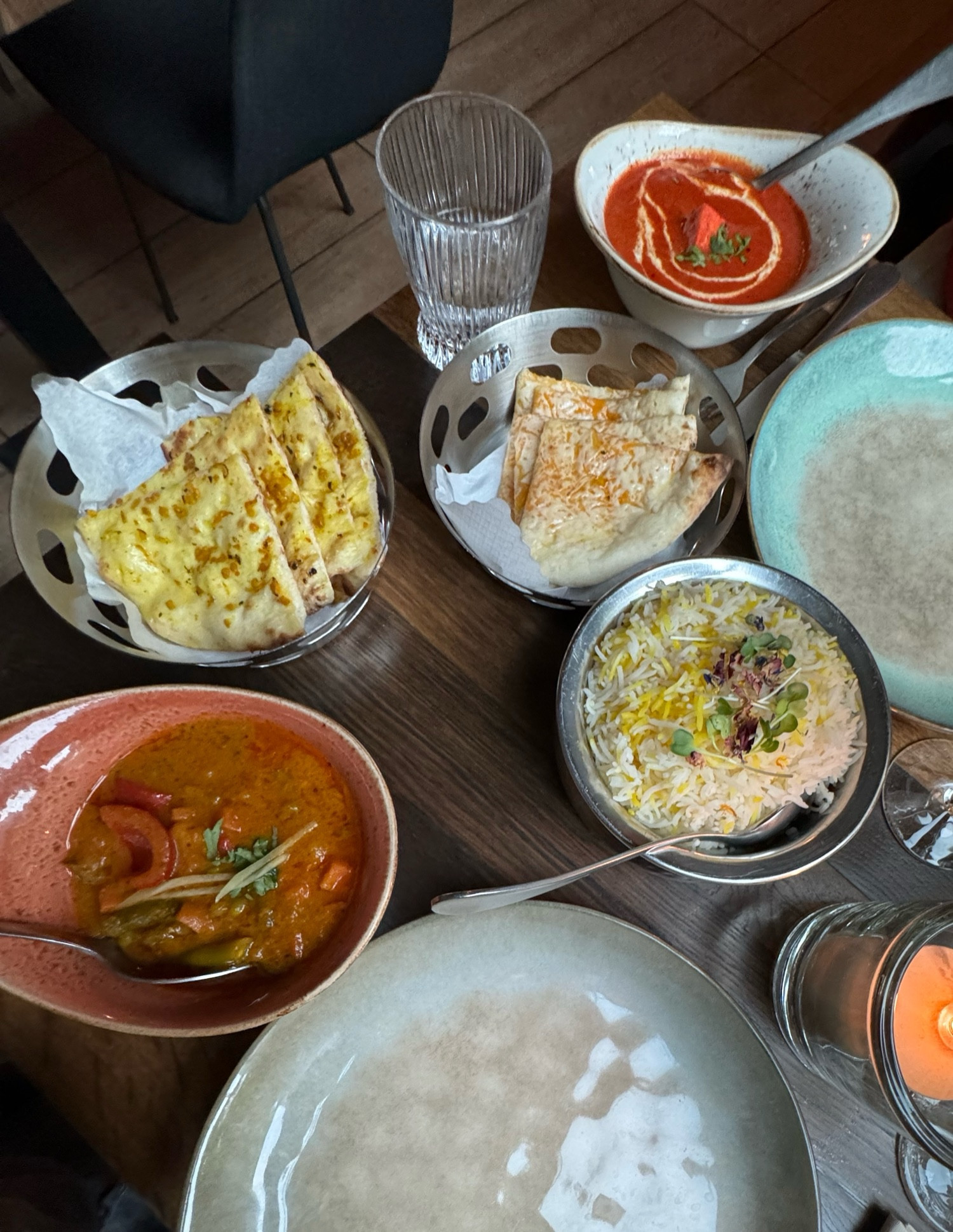 Schüsseln mit Reis, zwei Currygerichten, Garlicnaan und Käsenaan, Teller und Gläser auf einem Tisch