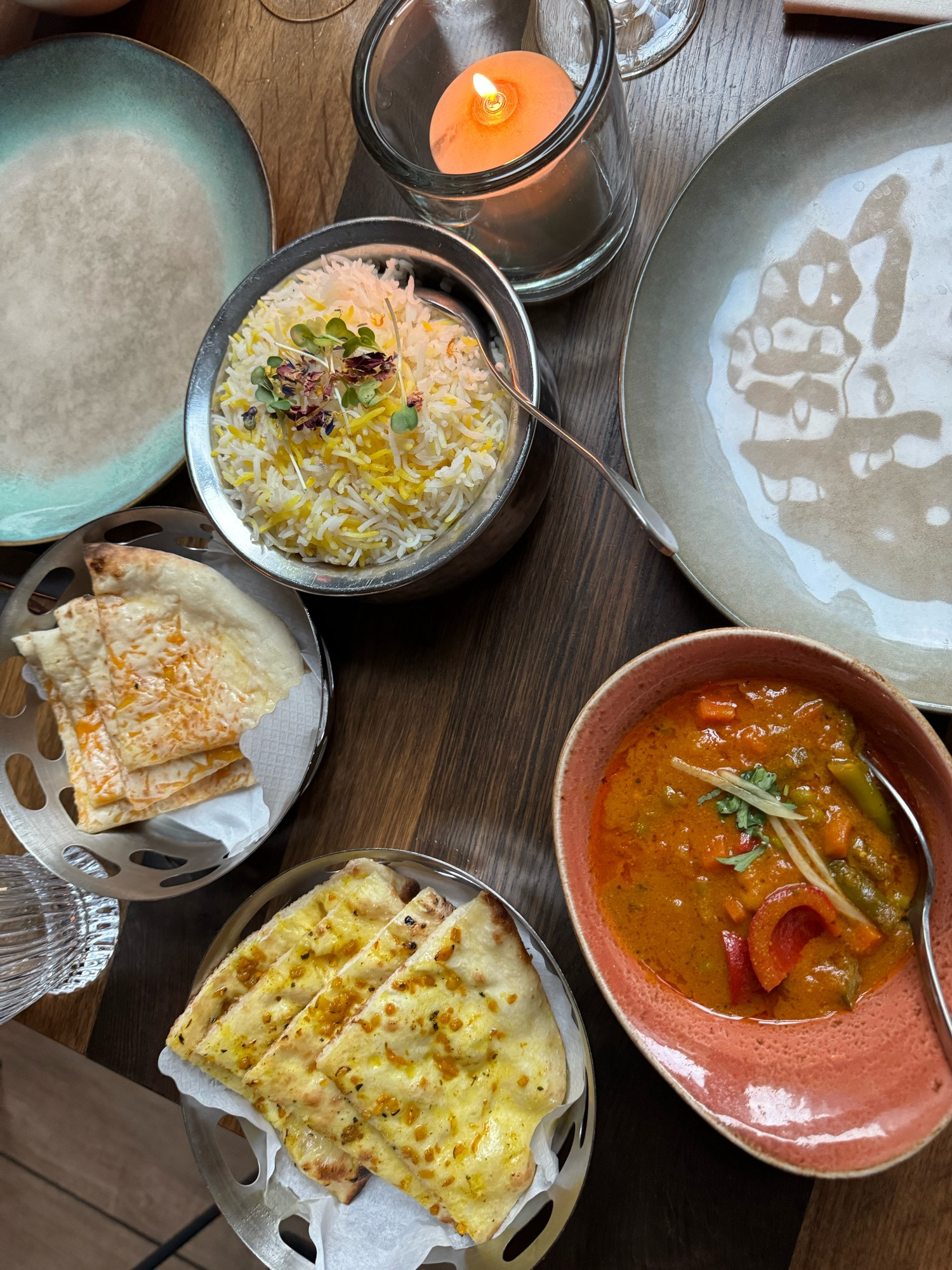 Ein Tisch von oben fotografiert, darauf zwei Schalen mit unterschiedlichen Naan-Broten, Reis und einem Currygericht