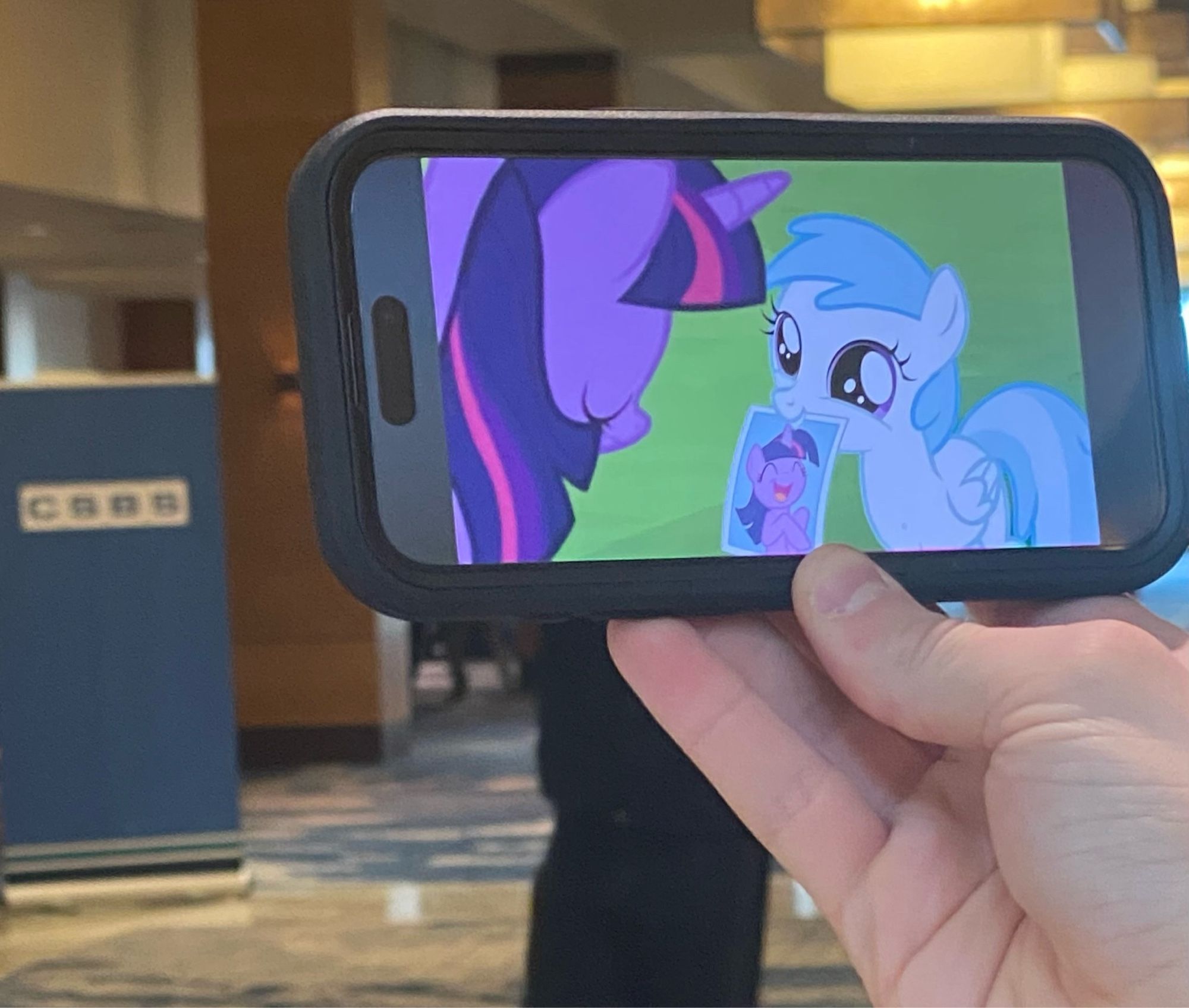 The end of Everfree Northwest in Seattle. A phone is being held up and shows an MLP: FiM episode against a backdrop of a business convention.