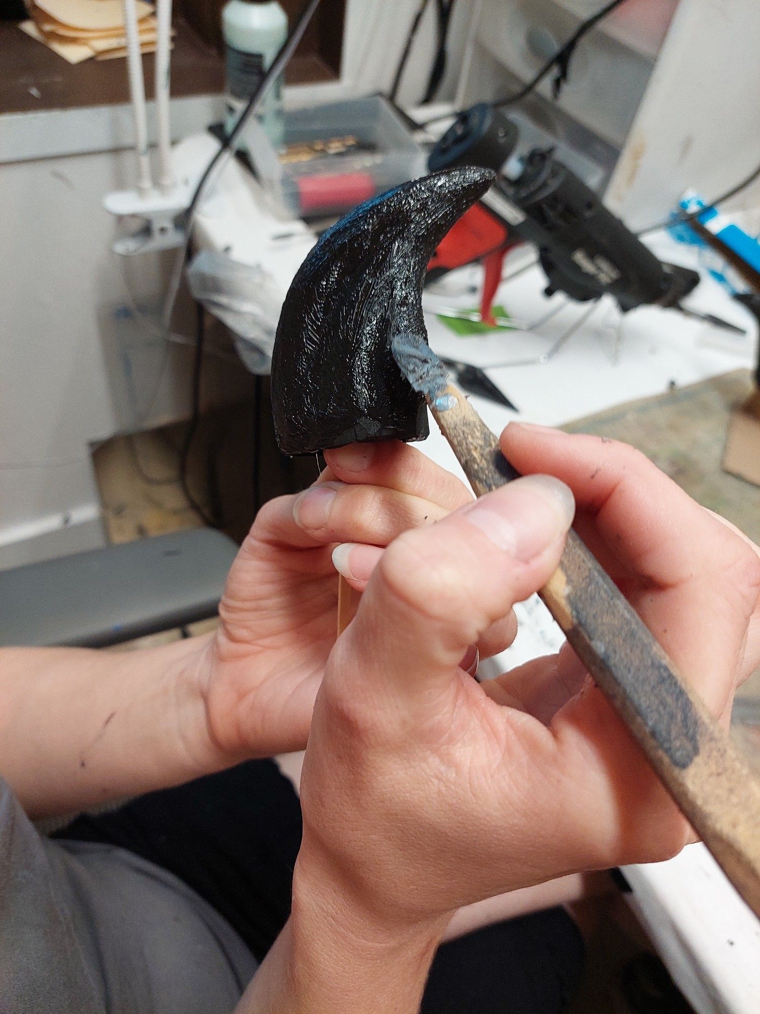 Shanzi's hands hold a large claw and a sculpting tool as she textures the claw's coating.