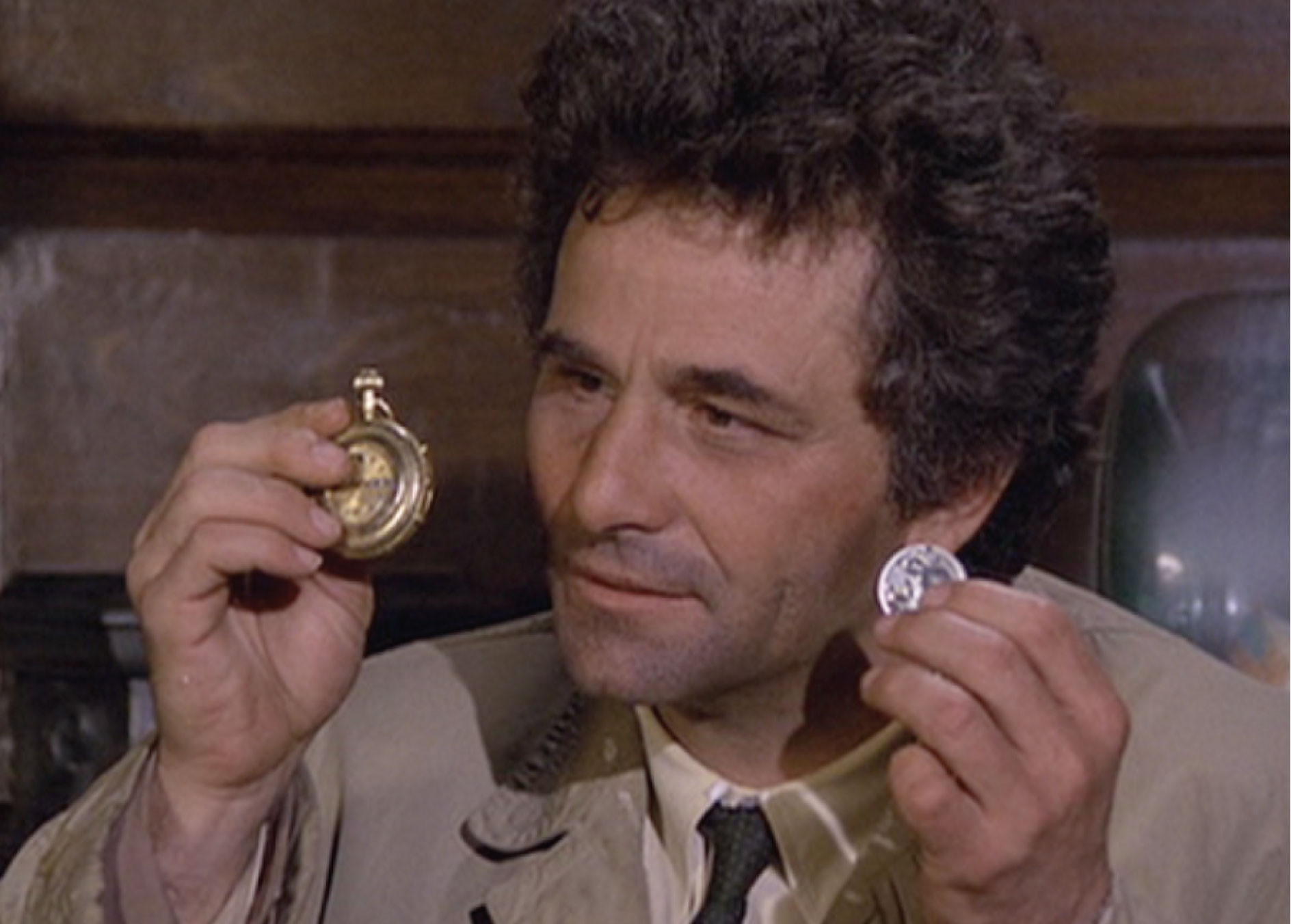 A close-up of Peter Falk as Lieutenant Columbo.  He is holding a gold pockewatch in one hand, and a silver coin in another. He is looking confused, as he is wont to do right before completely embarrassing a rich asshole.