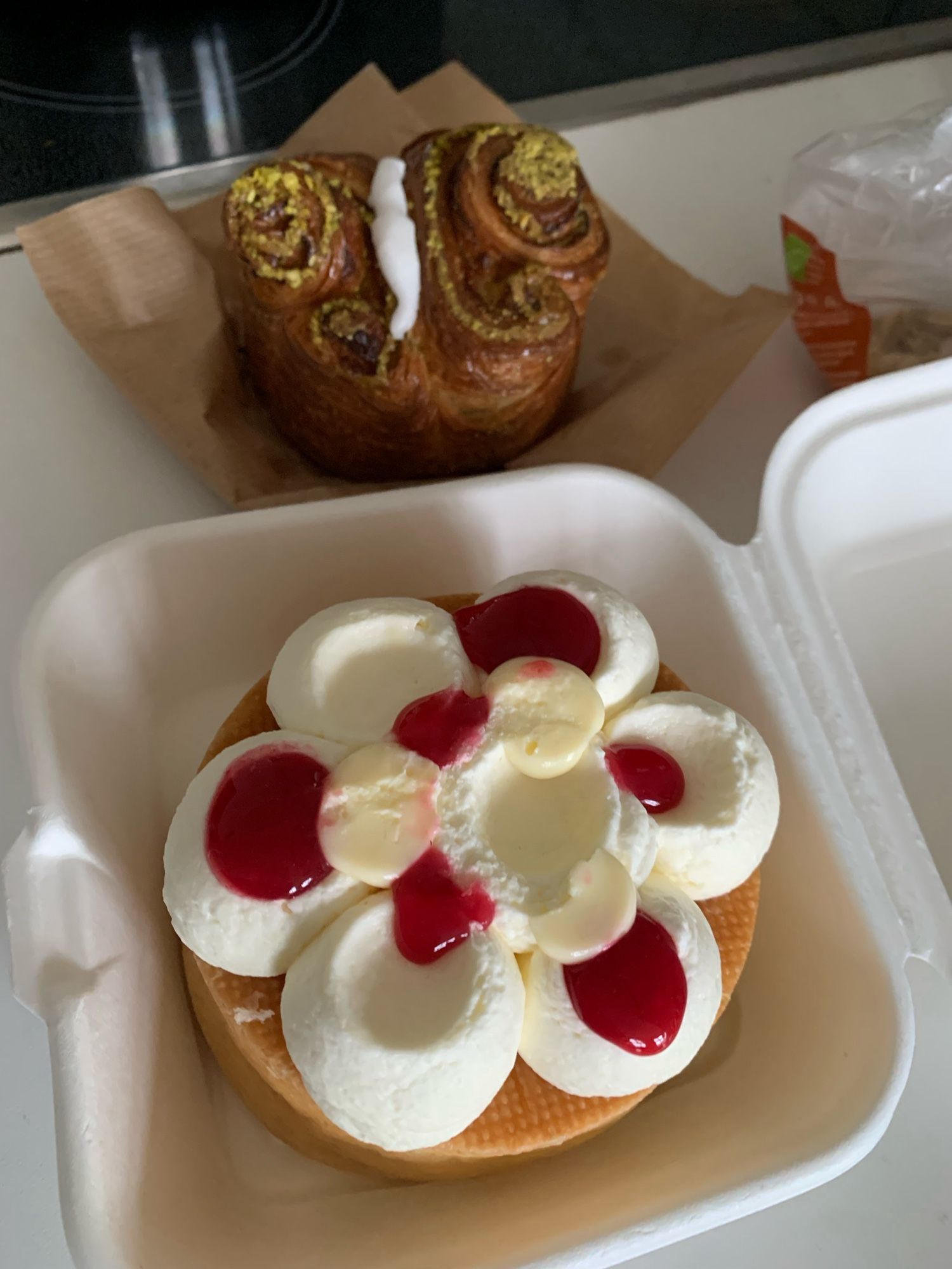 Vorn im Bild ein Baba, verziert mit Sahne und Erdbeermarmelade. Dahinter steht ein Pistachio Praline Brioche