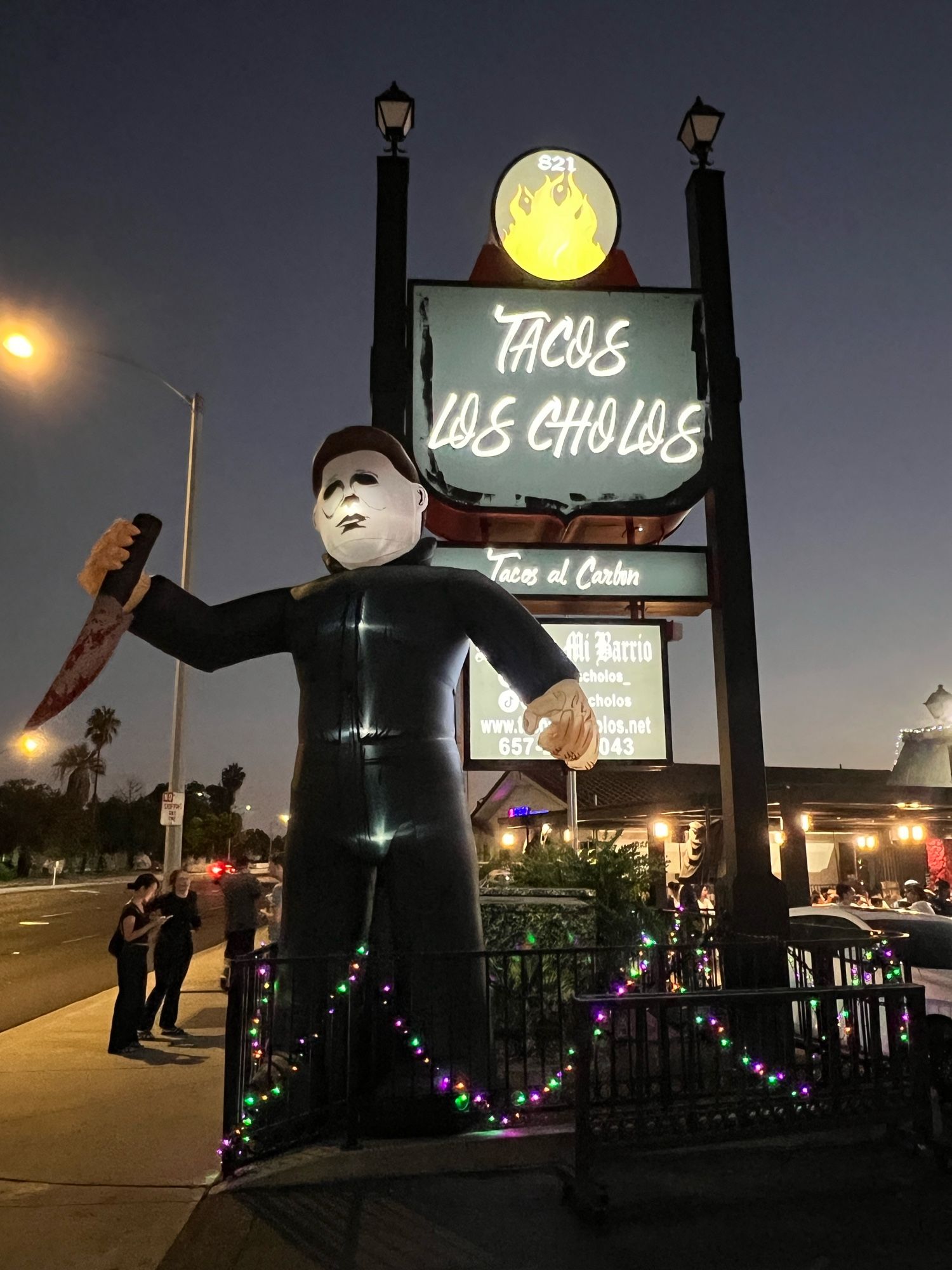 Sign for Tacos Los Cholos restaurant. With Halloween decorations.