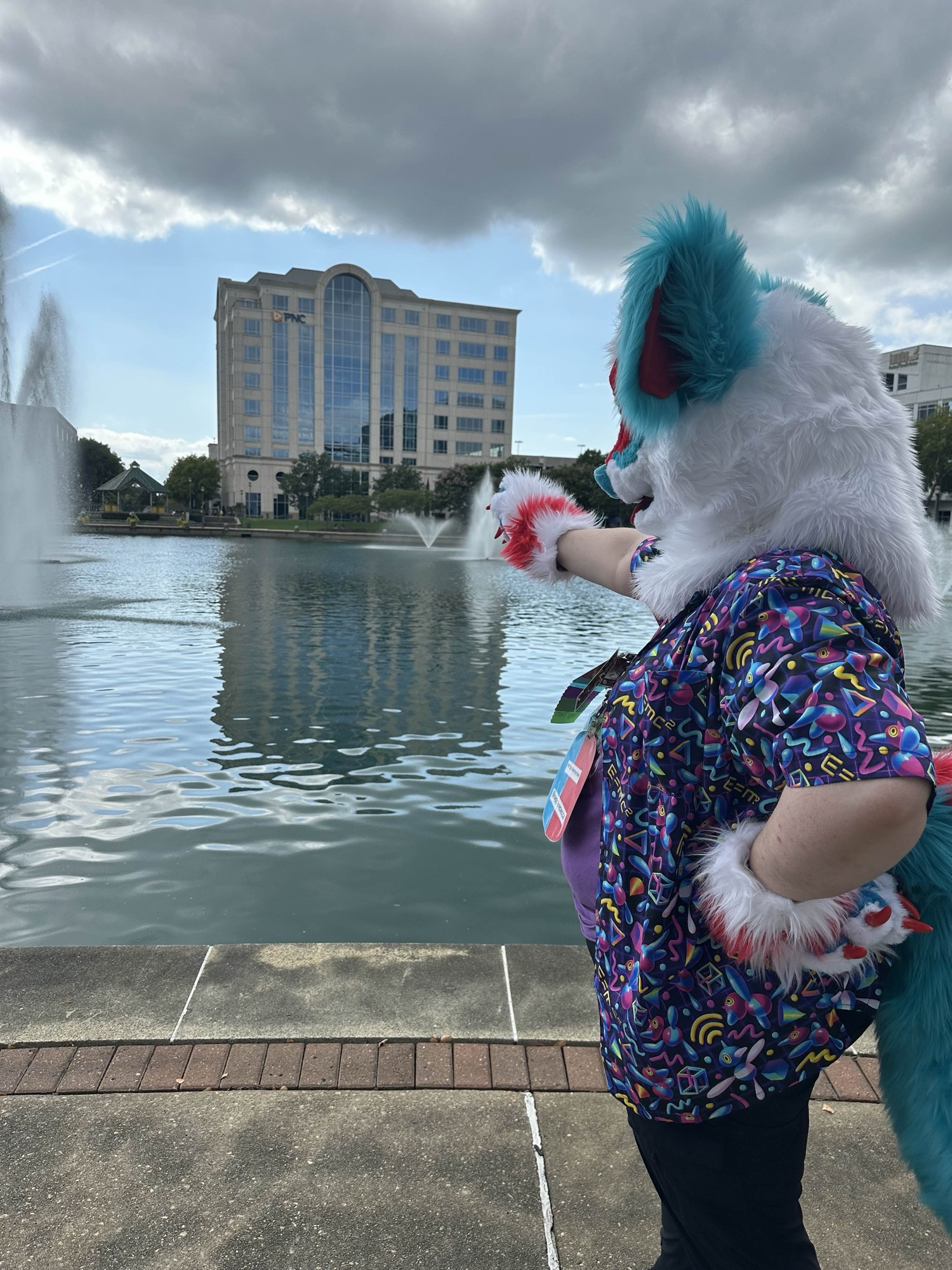 fursuiter points at fountain in a cityscape 