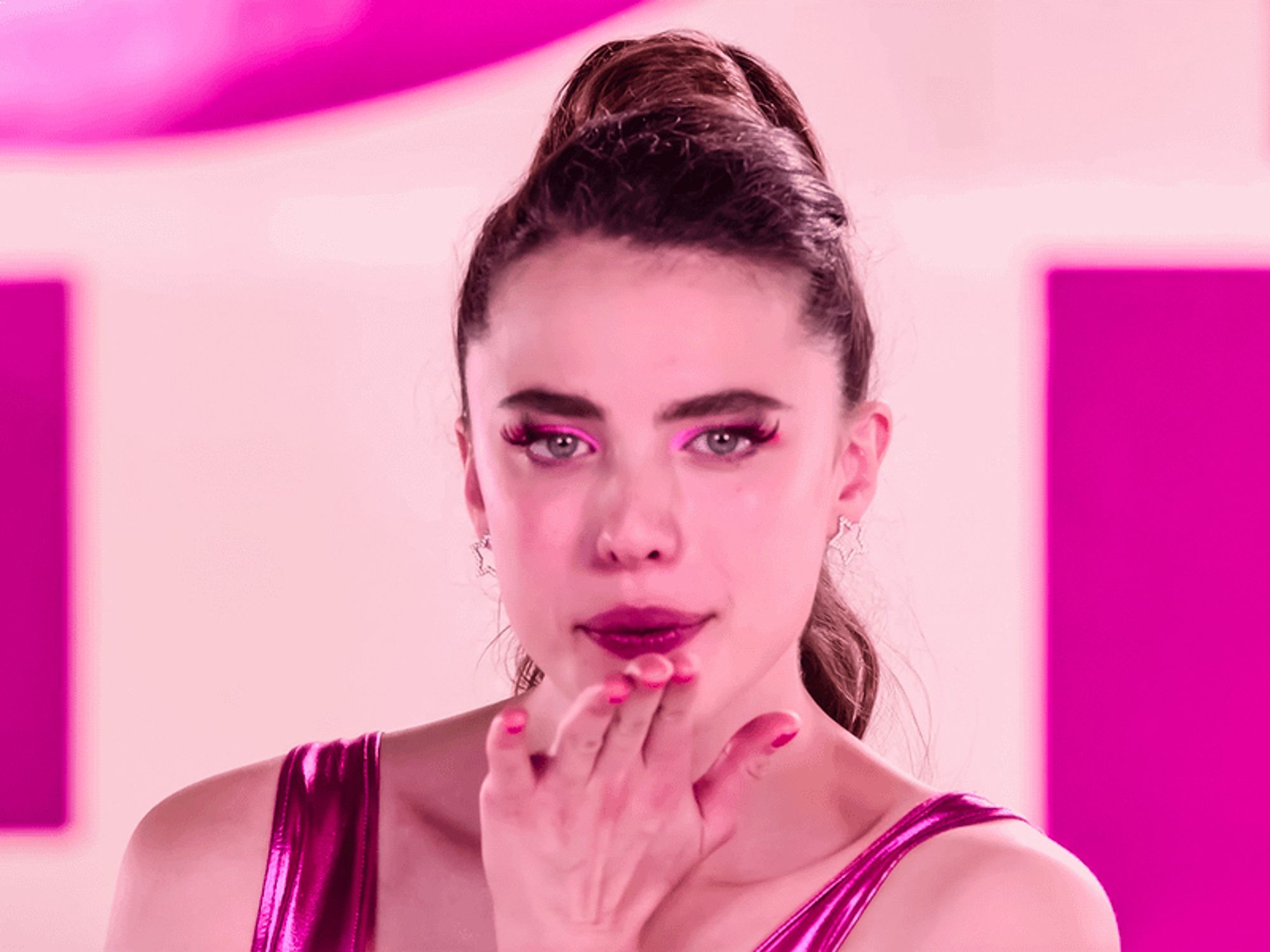 Screenshot of Sue from the Substance. She wears a pink leotard, pink eyeliner and lipstick, and blows a kiss towards the camera.