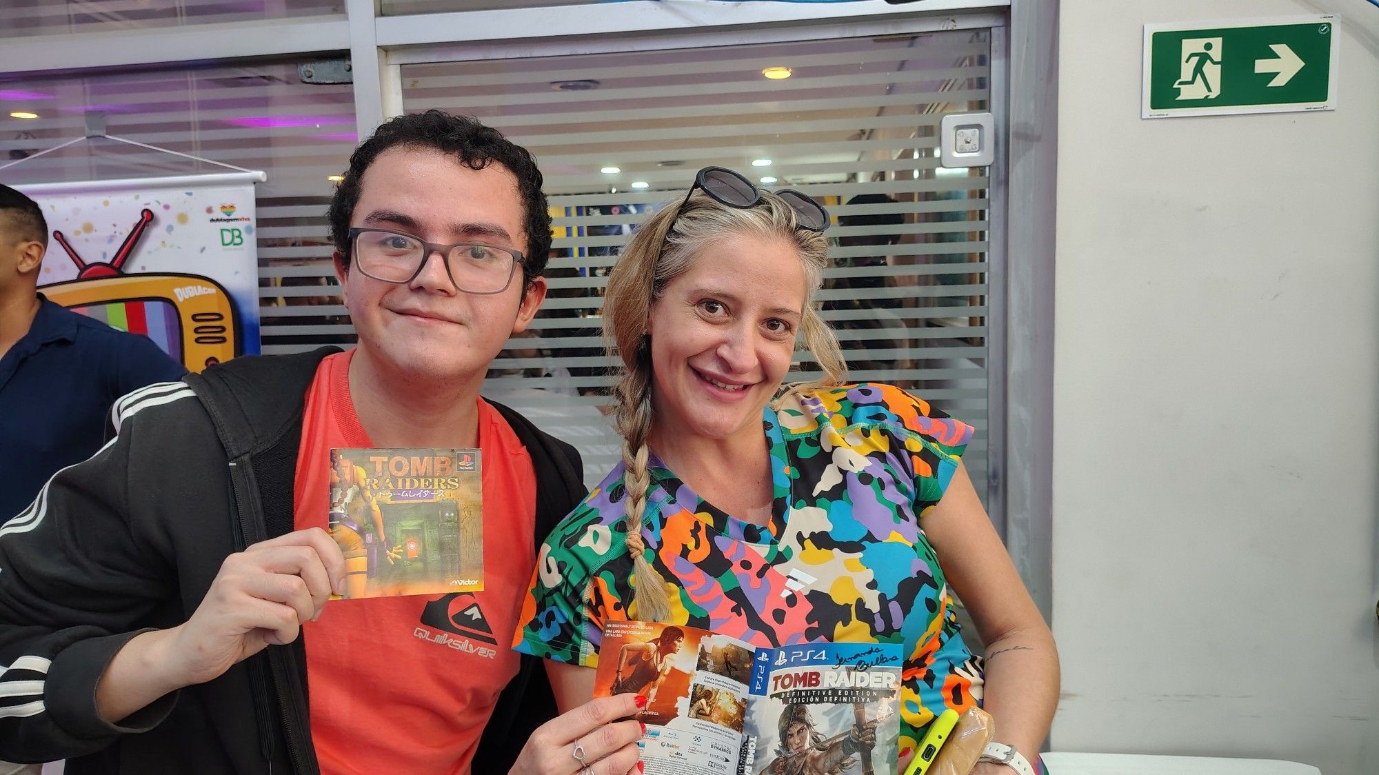 Na foto aparece o Yuri Suetsugu (integrante da WDN) e a dubladora Fernanda Bullara (voz da Tomoyo Daidouji, Lara Croft e outras personagens icônicas) segurando capas e manuais dos jogos de Tomb Raider.