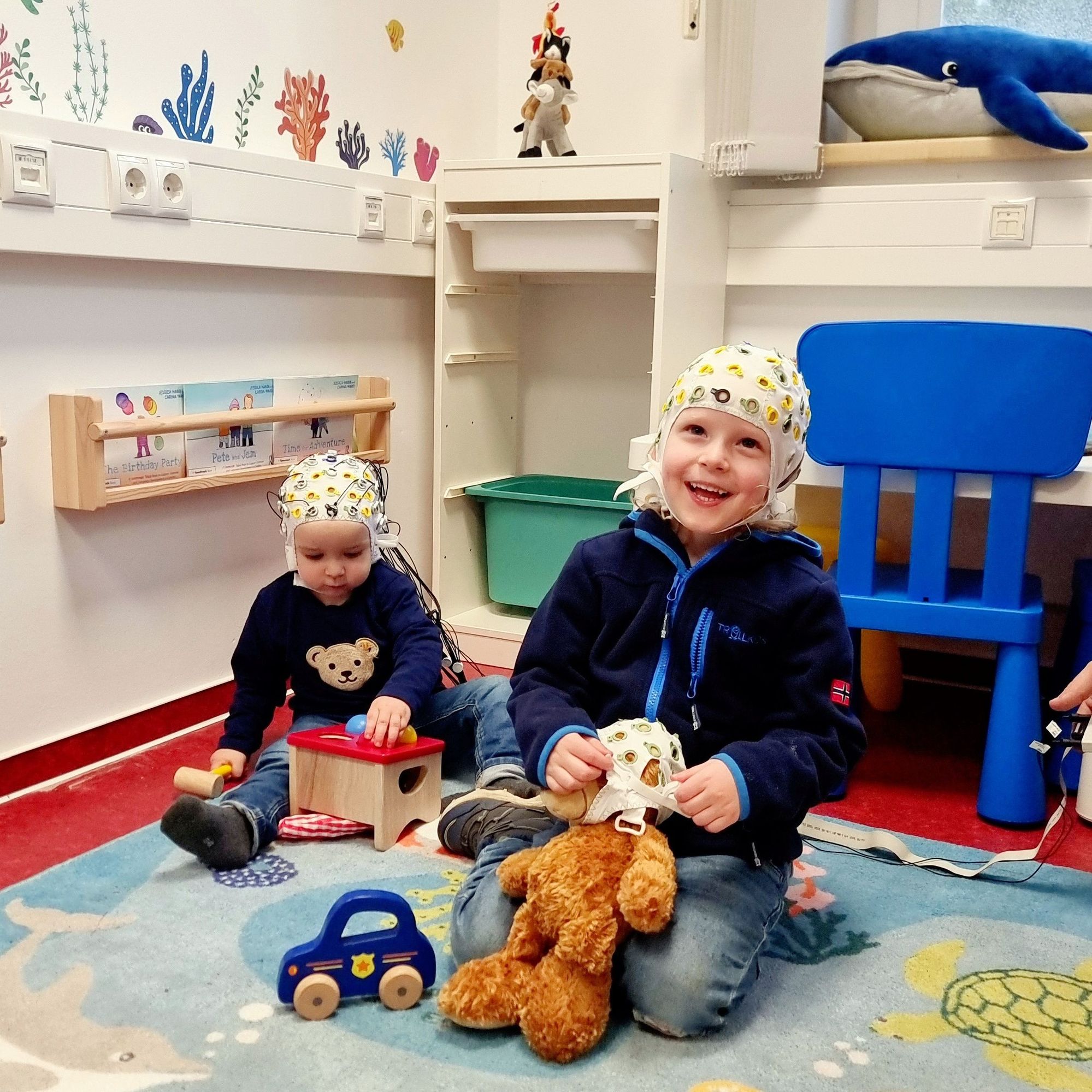 Two children wearing EEG caps, playing with toys