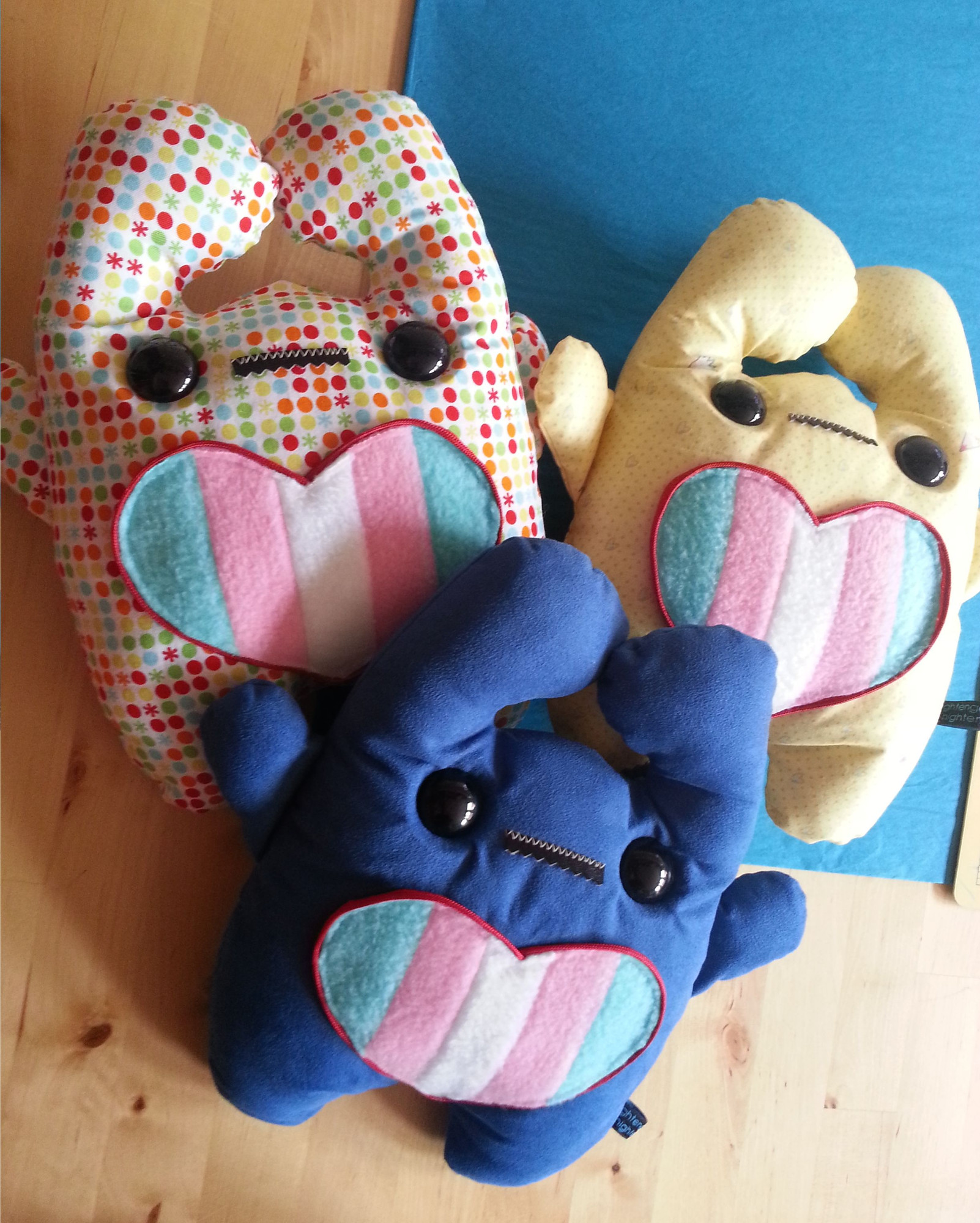 These early Pride Pals, from back in 2014, look pretty stressed out! 😨 

Their hearts used to be sewn onto the Pal back then, which made customizing a lot harder, and their Pride flags were made of fleece sewn together instead of custom printed minky like they are now. Plus, Pals these days smile a lot more 😁

Making the hearts a separate item instead of sewn onto the Pals' bellies also opened an opportunity for Shoulder Pets to hold the hearts too!