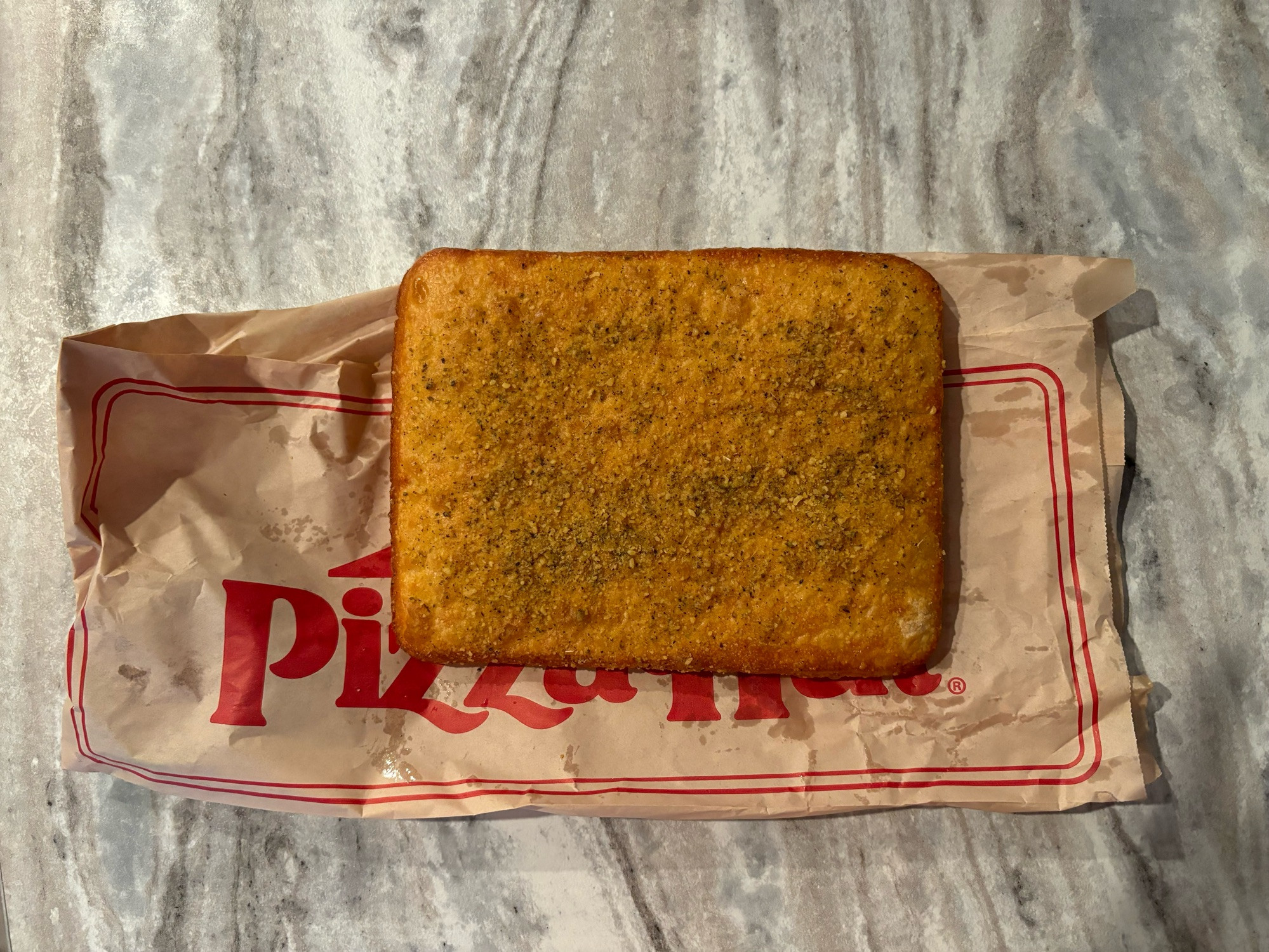 An uncut square of breadstick bread on a brown wrapper from Pizza Hut.