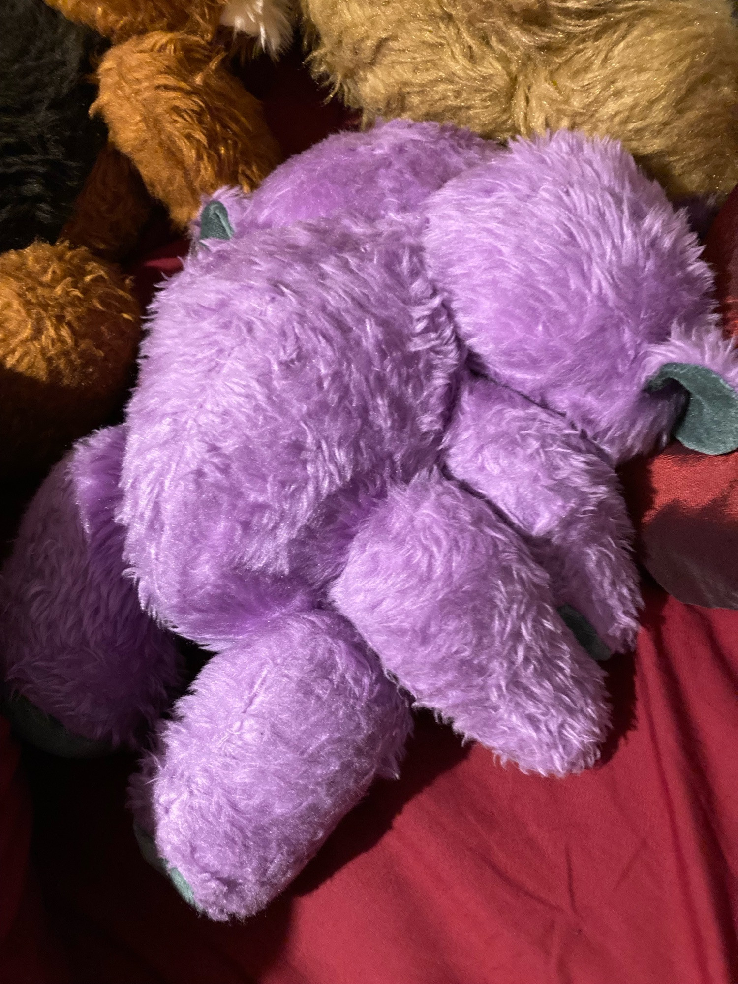 back view of 2 headed purple bear lying face down on red duvet