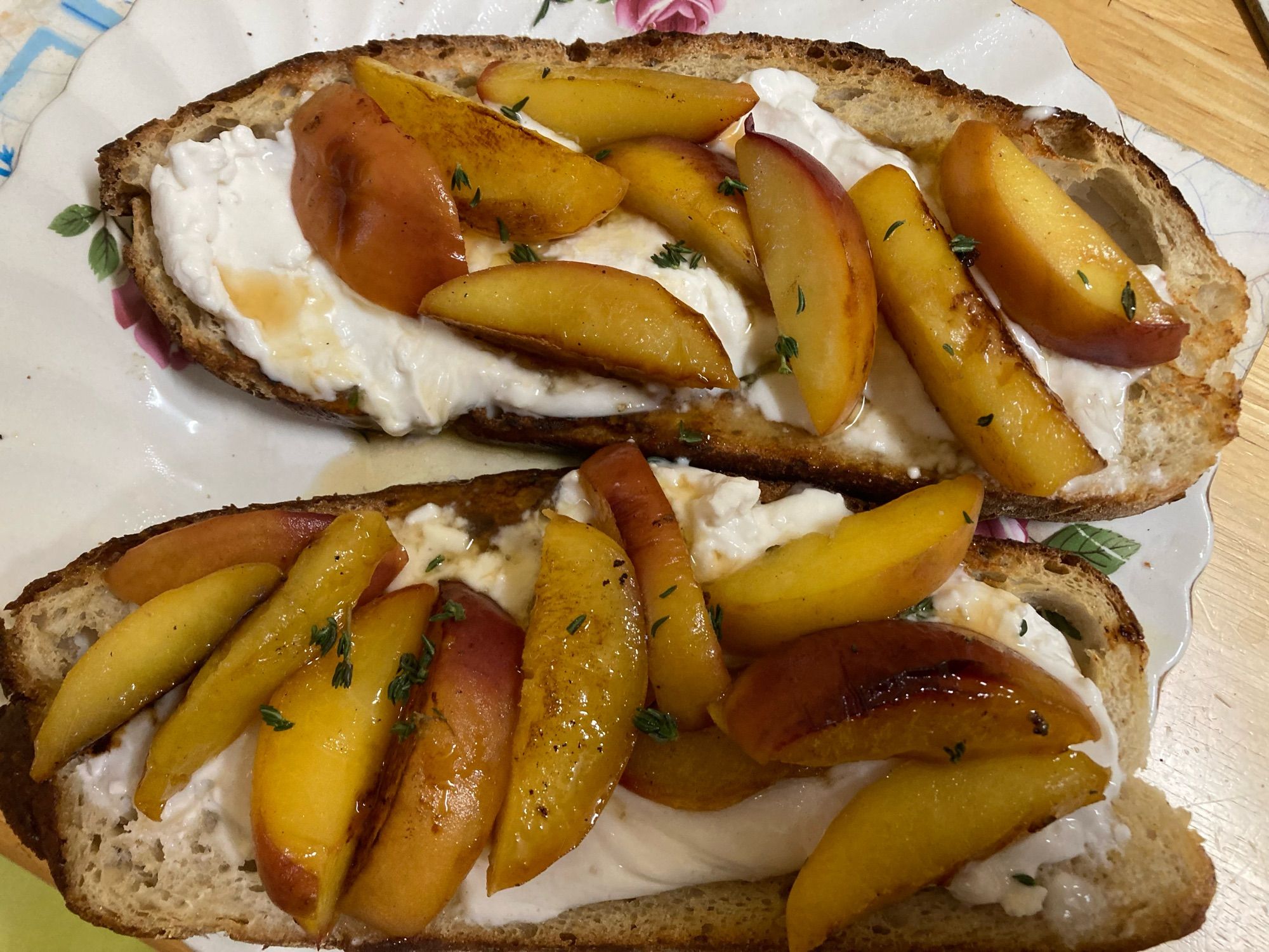 2 slices of bread on plate with vegan cheese, peach slices and thyme, agave syrup and olive oil