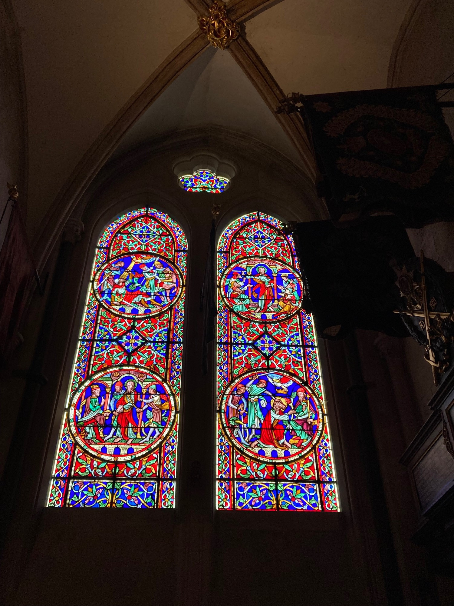 dual panel stained glass window in Chichester Cathedral set in arch window shape. Dominant colour is red, but also plenty of royal blue. The arch which it is situated is in low light.