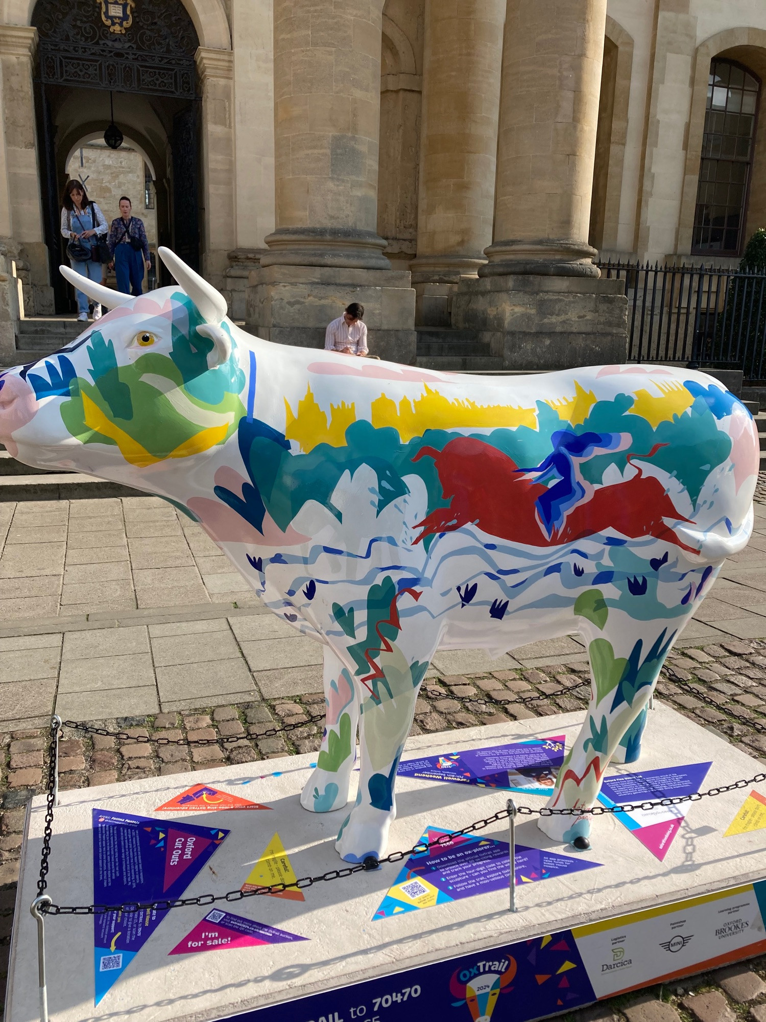 side view of ox sculpture, white with city outline painted in yellow, woman riding a horse in red