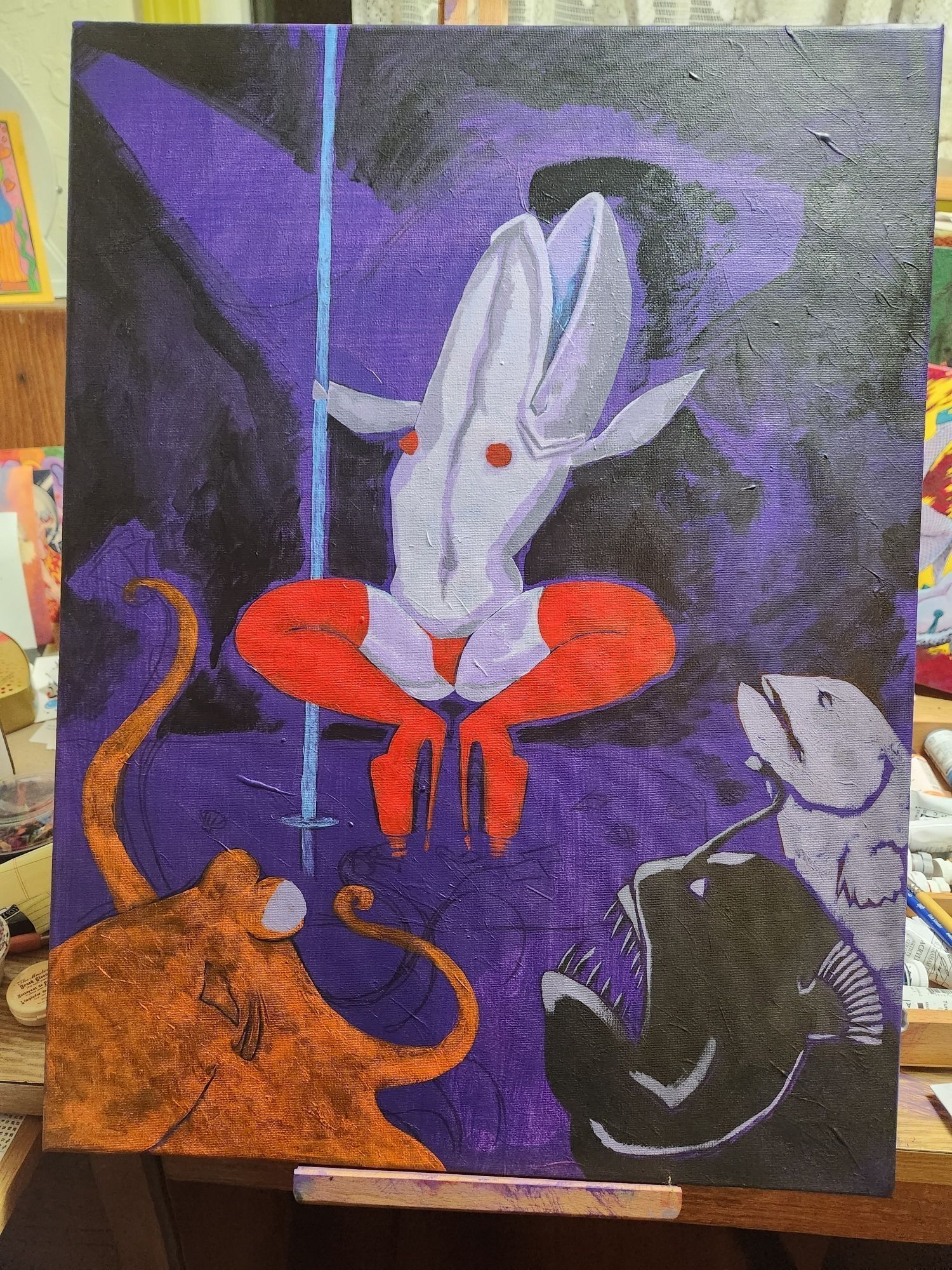 A photo of a painting in progress sitting on an easel. A reverse mermaid on a stage next to a pole in thigh high red stripper boots. An octopus and an angler fish and a grouper can be seen sitting in the foreground in the lower third.