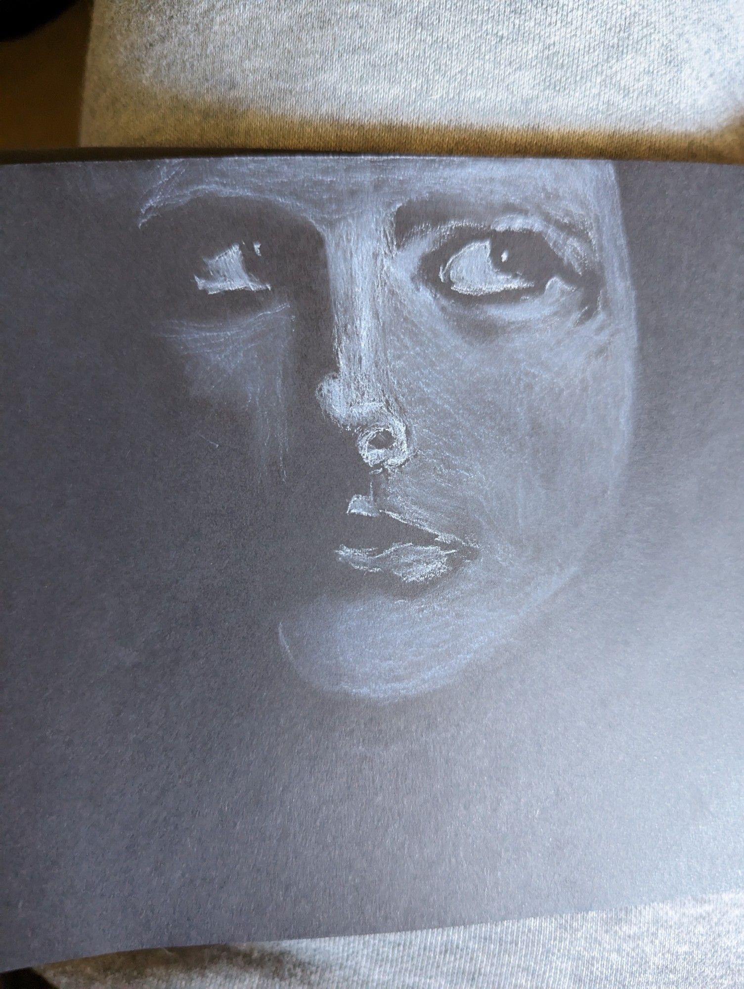 White chalk drawing of a person's face eyes to the side. Mostly shadowed. Done on black paper