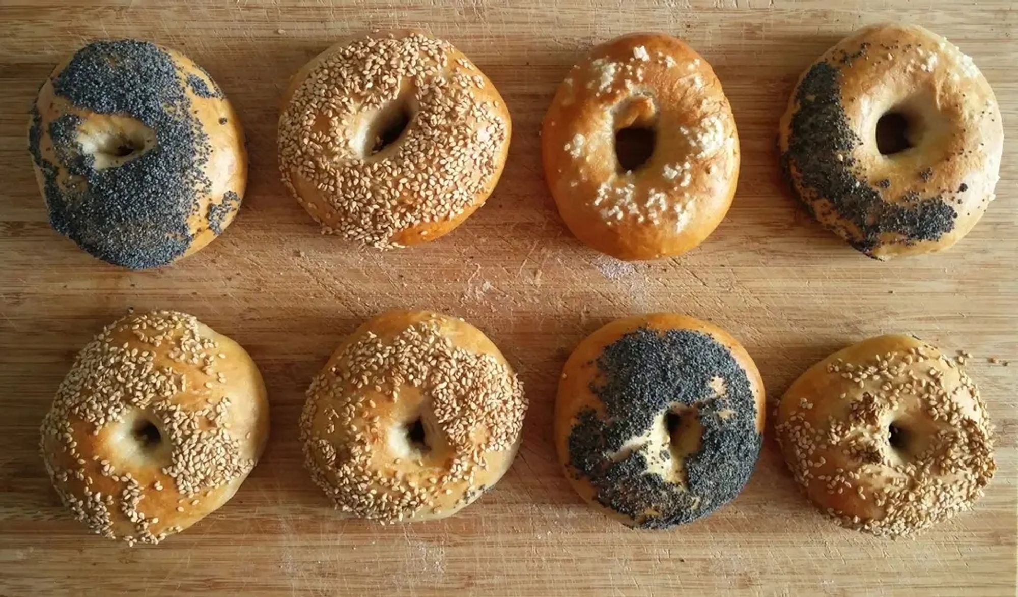 Eight bagels on a bread board.