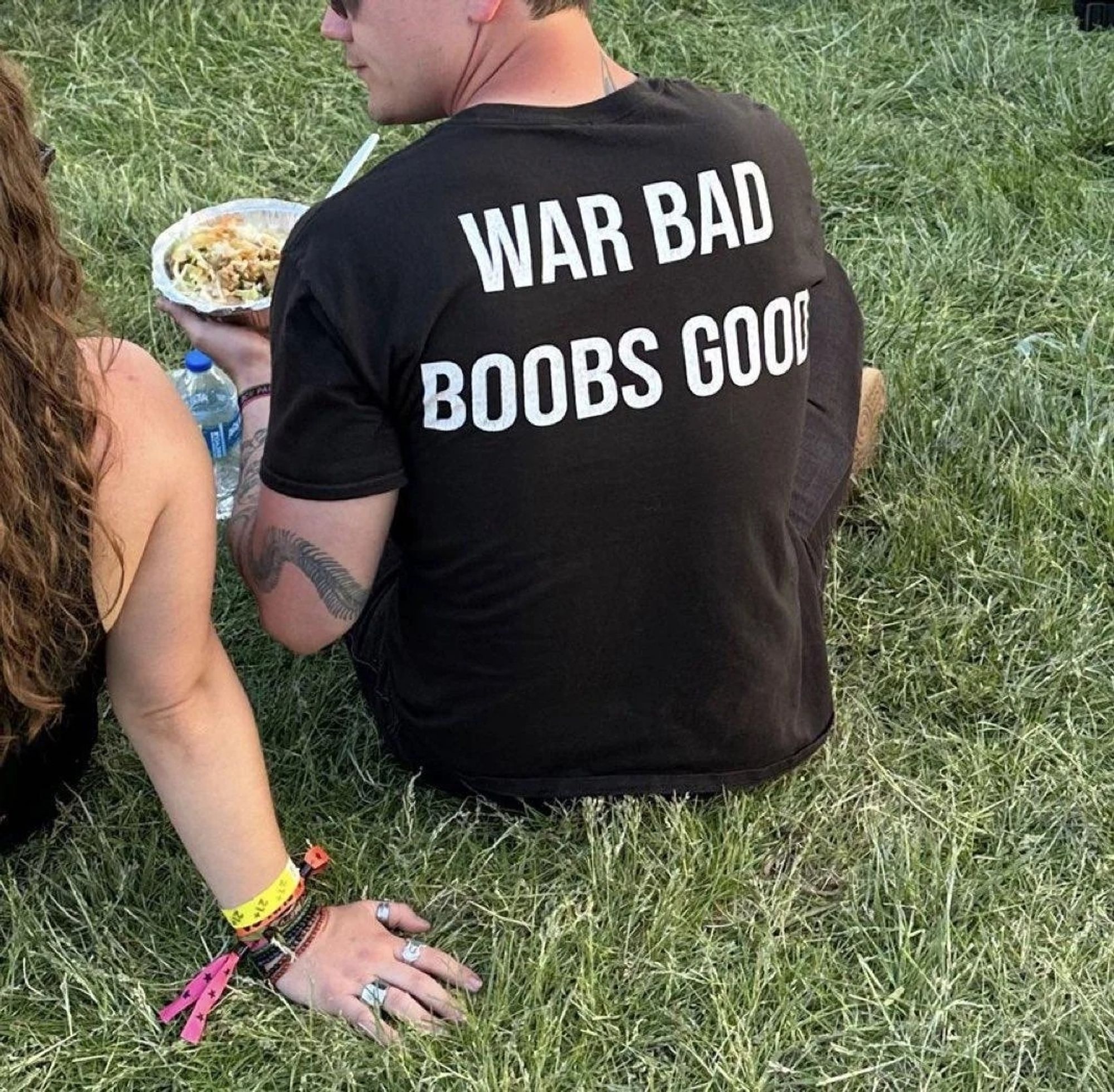 A man wearing a black T-shirt with big words on the back that read "war bad, boobs good."