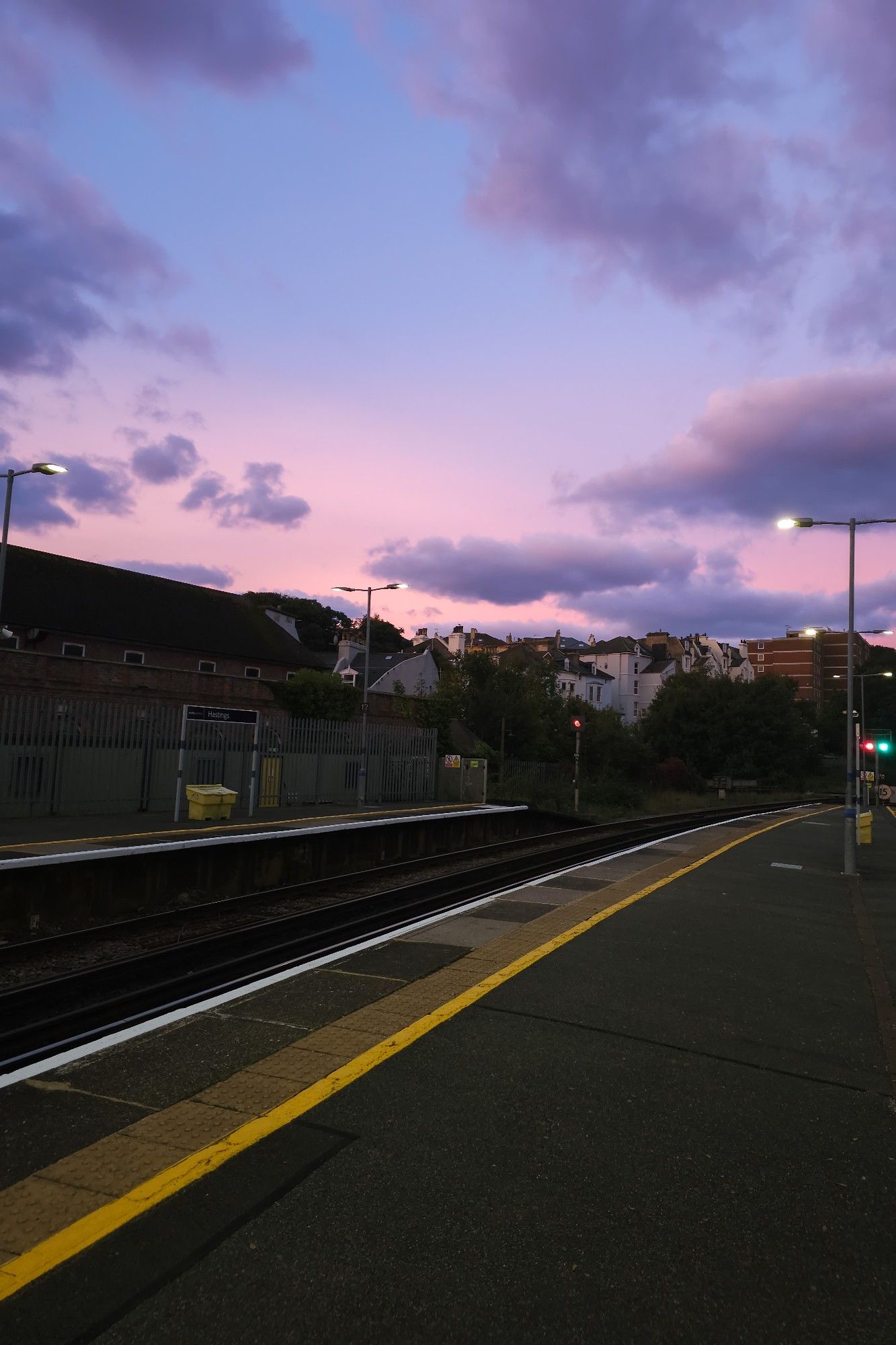 A train platform with a pinkish sky fading to blue with fluffy clouds.