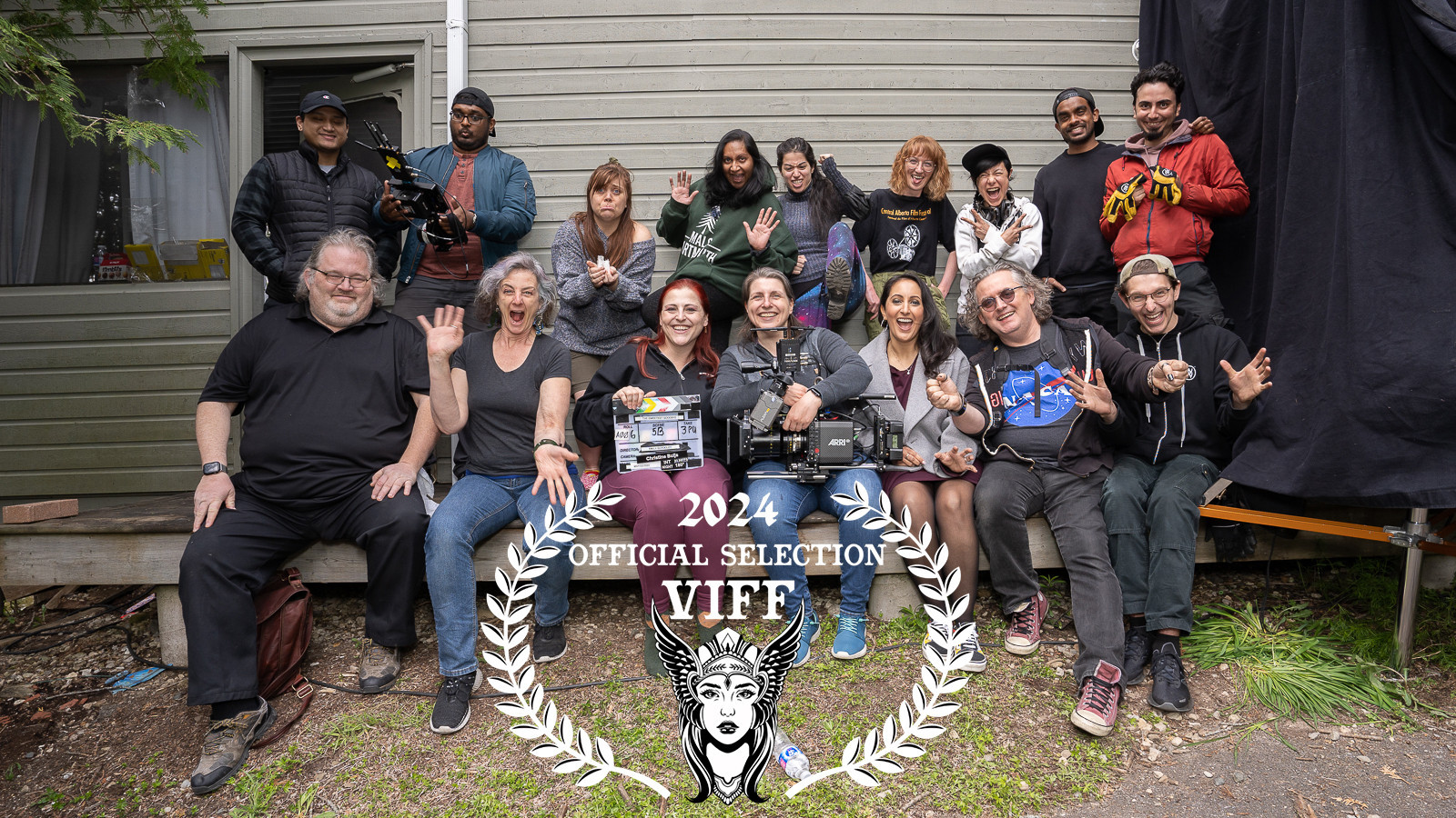 The cast and crew of the short film The Sweetest Goodbye. Sixteen people of diverse backgrounds sit outside on a wooden patio. Everyone is facing toward camera with excited expressions.