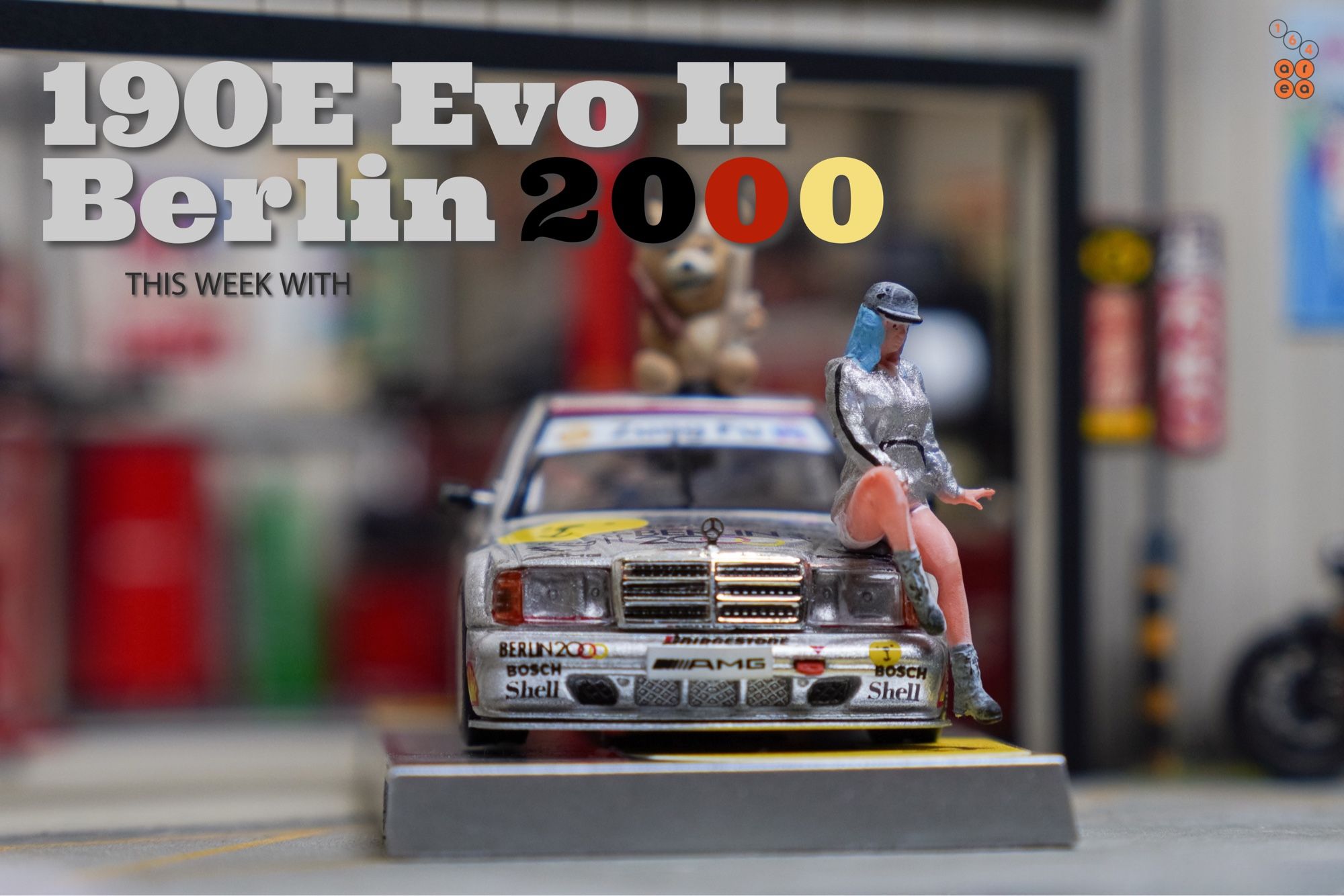 A Ted bear and female in silver suit sit on Mercedes-Benz 190E 2.5-16 Evolution II, Berlin 2000 livery by Tarmac Works in 1:64 scale with 1:64 figures on AREA 164