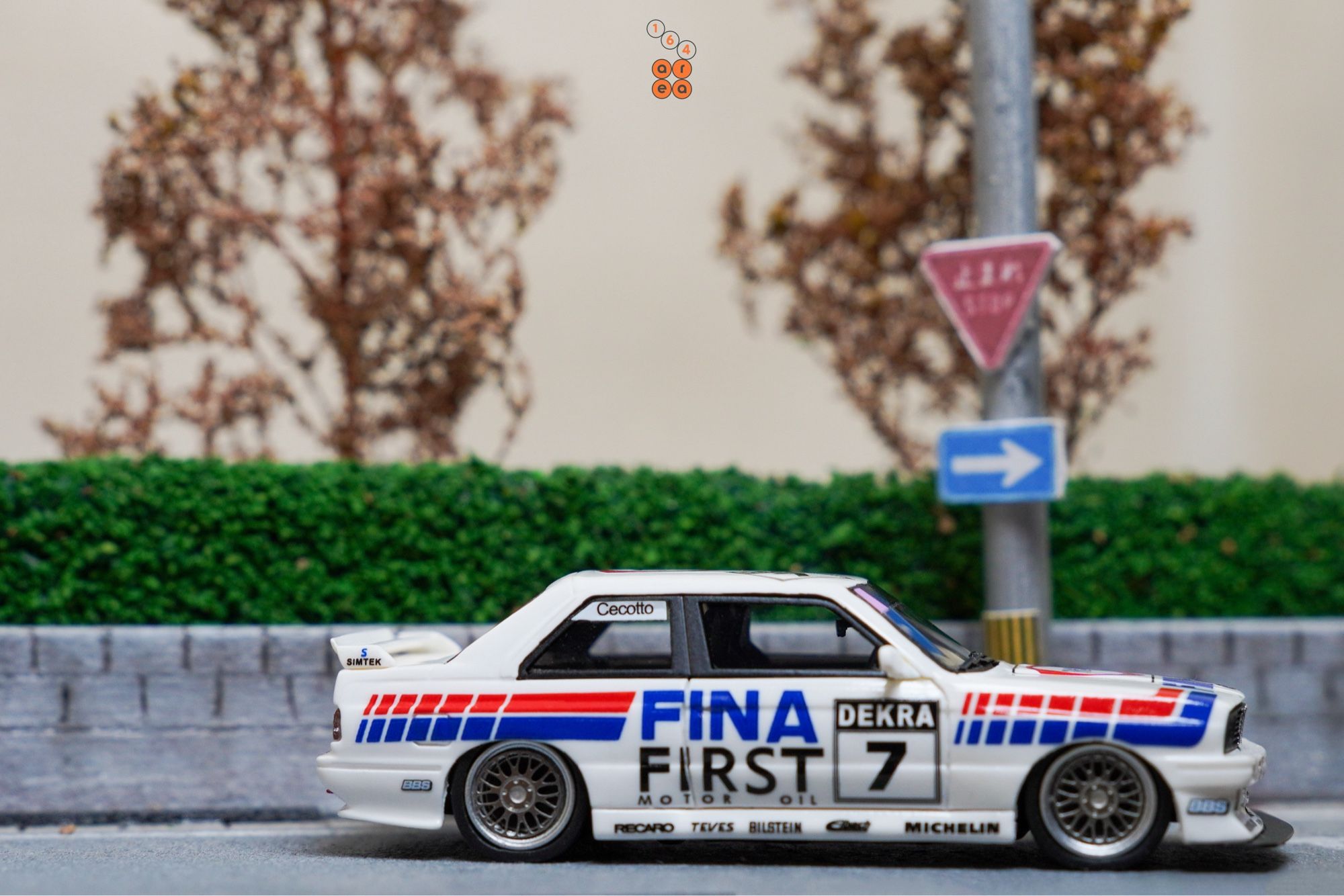 A turn right sign and a right side of BMW E30 M3, FINA First Oil livery by ScaleMini in 1:64 scale on AREA 164