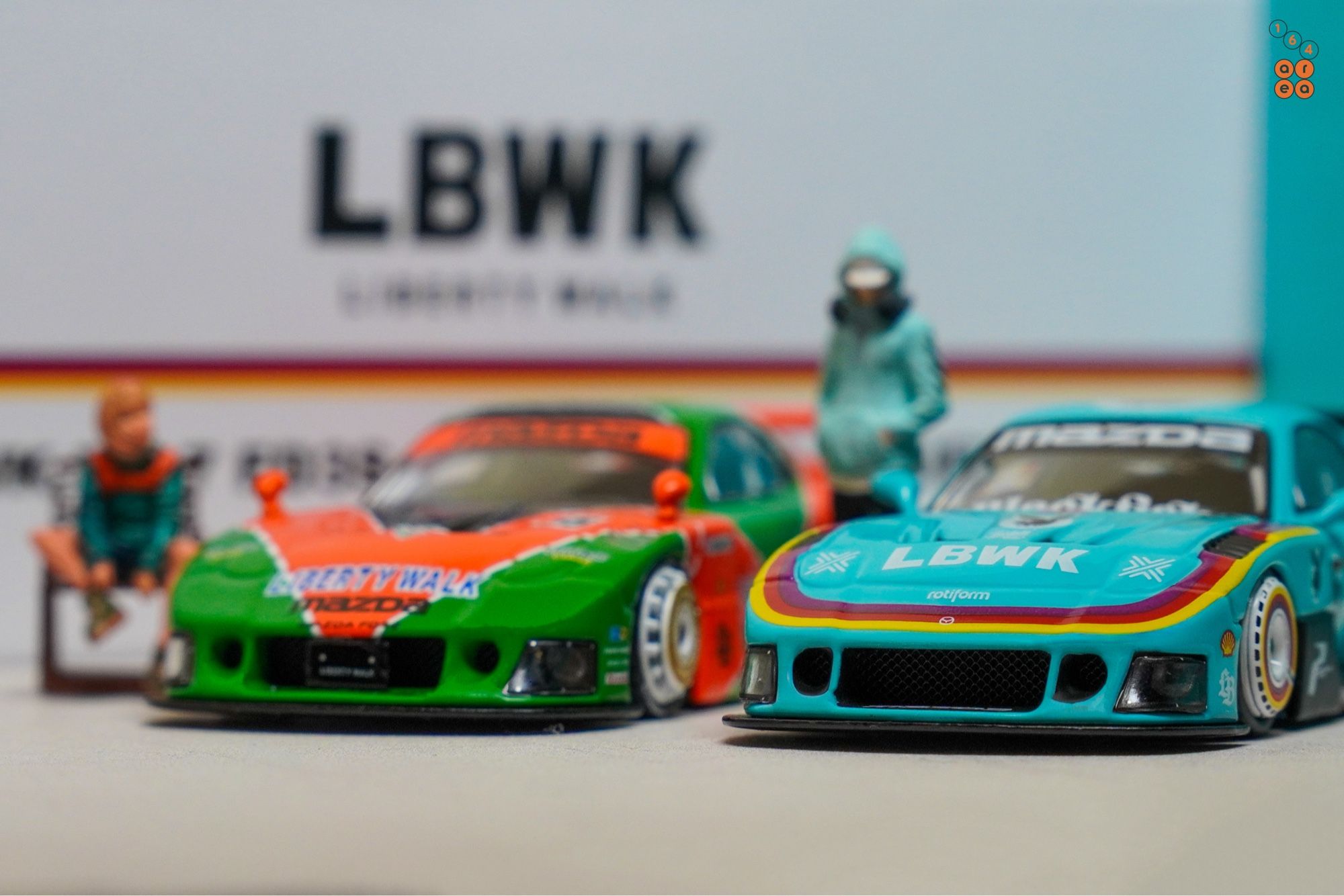 A front side of Mazda RX-7 FD3S, LB-Super Silhouette, Hobby Expo China 2024 Edition beside a Renown livery, both by iNNO64 in 1:64 scale with 1:64 figure on AREA 164