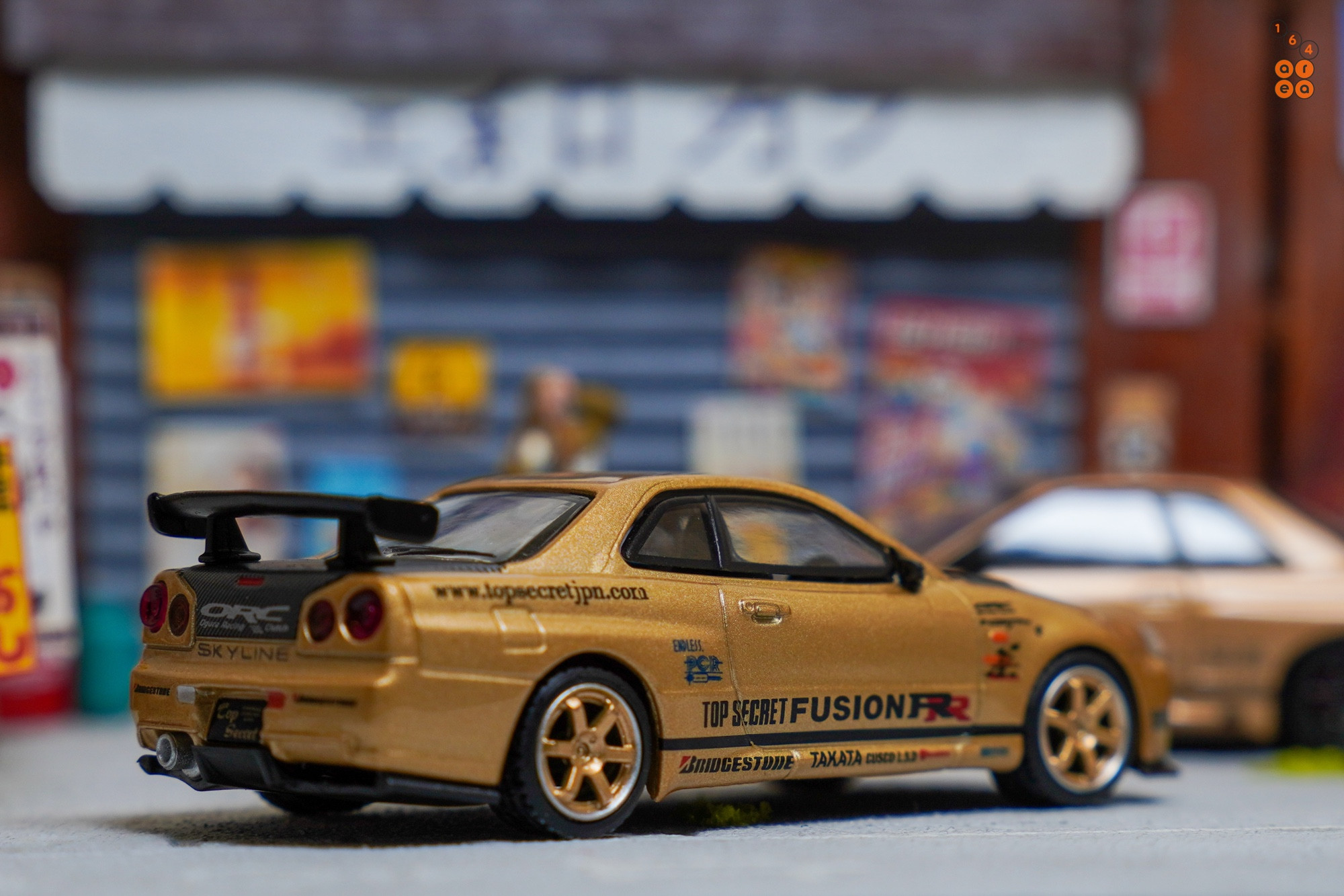 A right side of Nissan Skyline GT-R (R34) Top Secret, Top Secret Gold by MINI GT in 1:64 scale on AREA 164