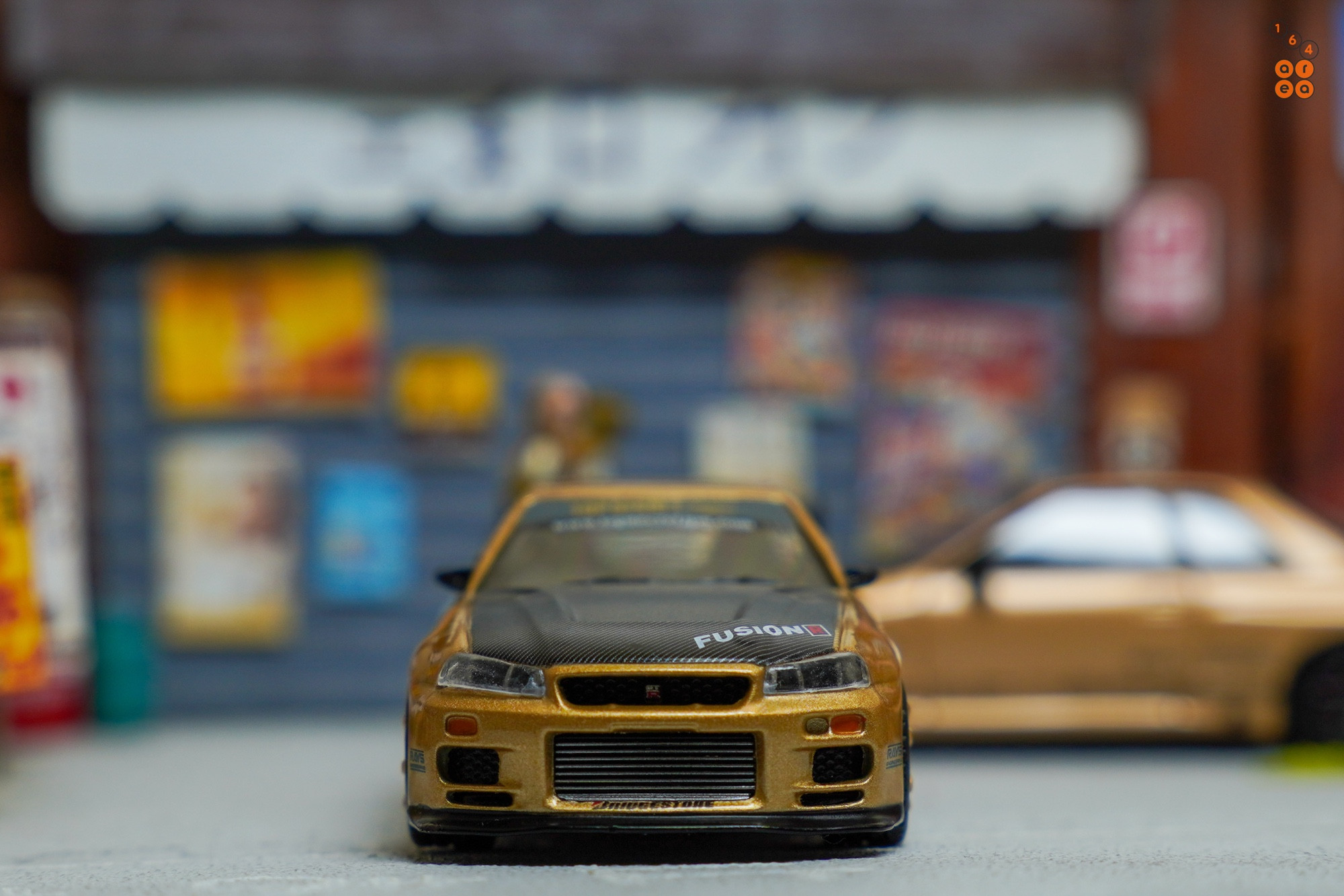 A front side of Nissan Skyline GT-R (R34) Top Secret, Top Secret Gold by MINI GT in 1:64 scale on AREA 164