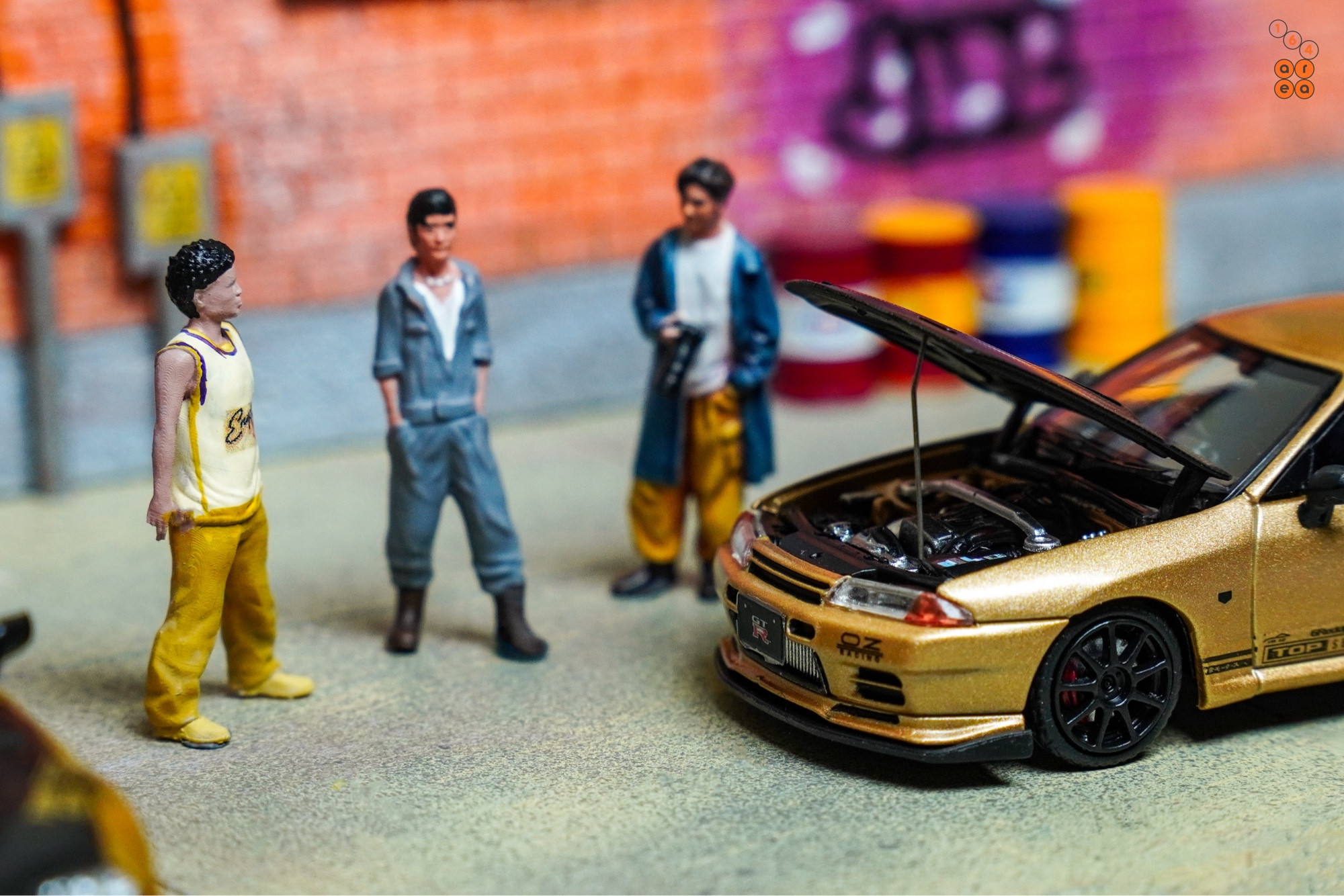 3 guys stand beside Toyota Supra A80 by Time Micro and Nissan Skyline GT-R VR32 by Facal Horizon, both with Top Secret Gold livery in 1:64 scale on AREA 164