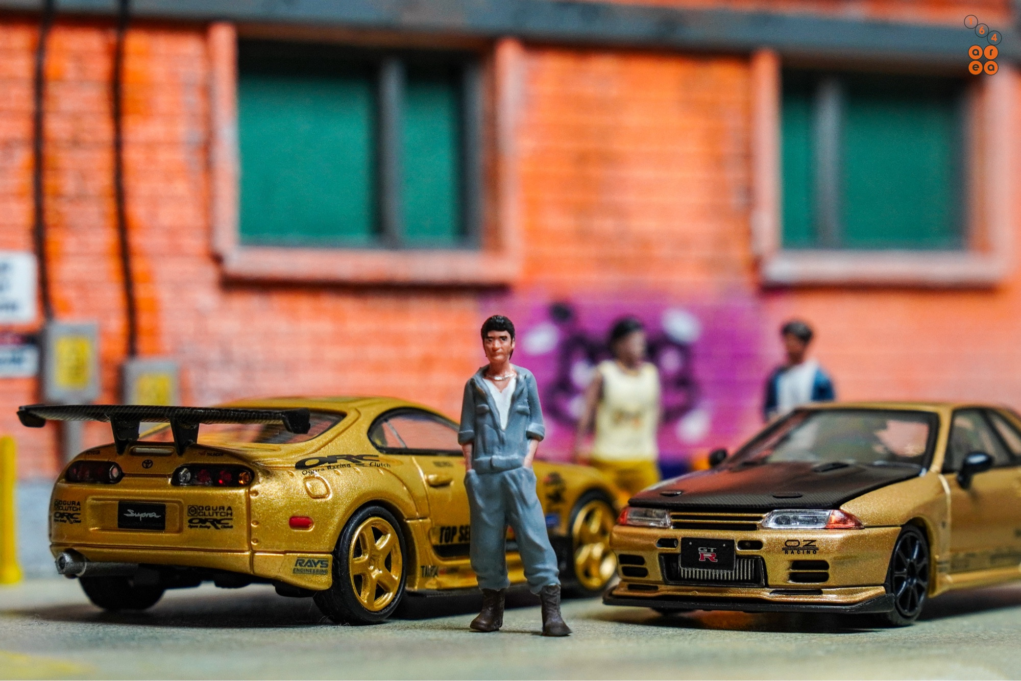 A guy stand in front of Toyota Supra A80 by Time Micro and Nissan Skyline GT-R VR32 by Facal Horizon, both with Top Secret Gold livery in 1:64 scale on AREA 164