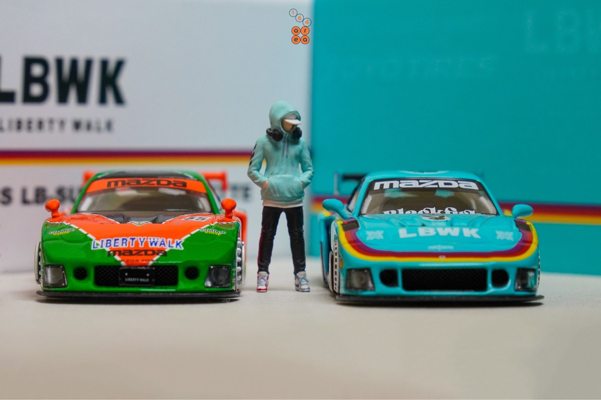 A front side of Mazda RX-7 FD3S, LB-Super Silhouette, Hobby Expo China 2024 Edition beside a Renown livery, both by iNNO64 in 1:64 scale with 1:64 figure on AREA 164