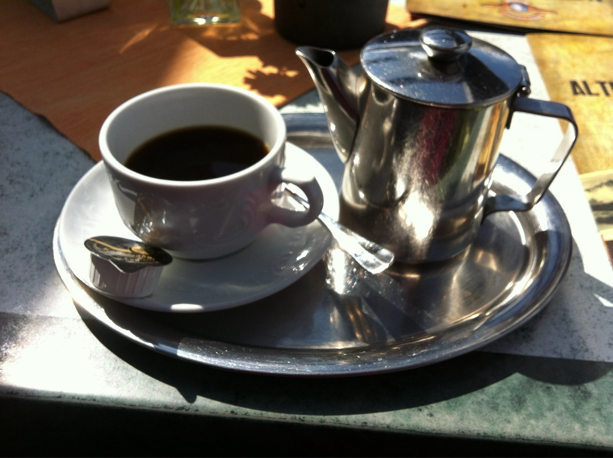 Kaffee-Gedeck auf silbernem Tablett mit silberner Kanne und weißer Kaffeetasse auf Unterteller. Die Sonne scheint von rechts oben ins Bild.